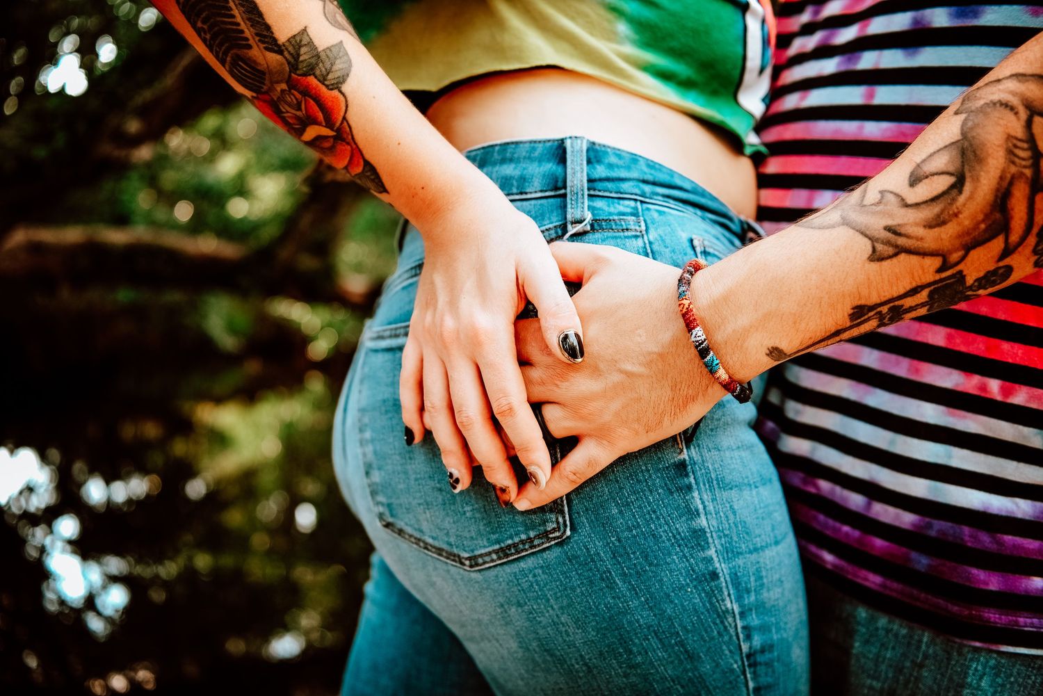 Close up view of hands resting on denim jeans showing tattoos and casual summer clothing.