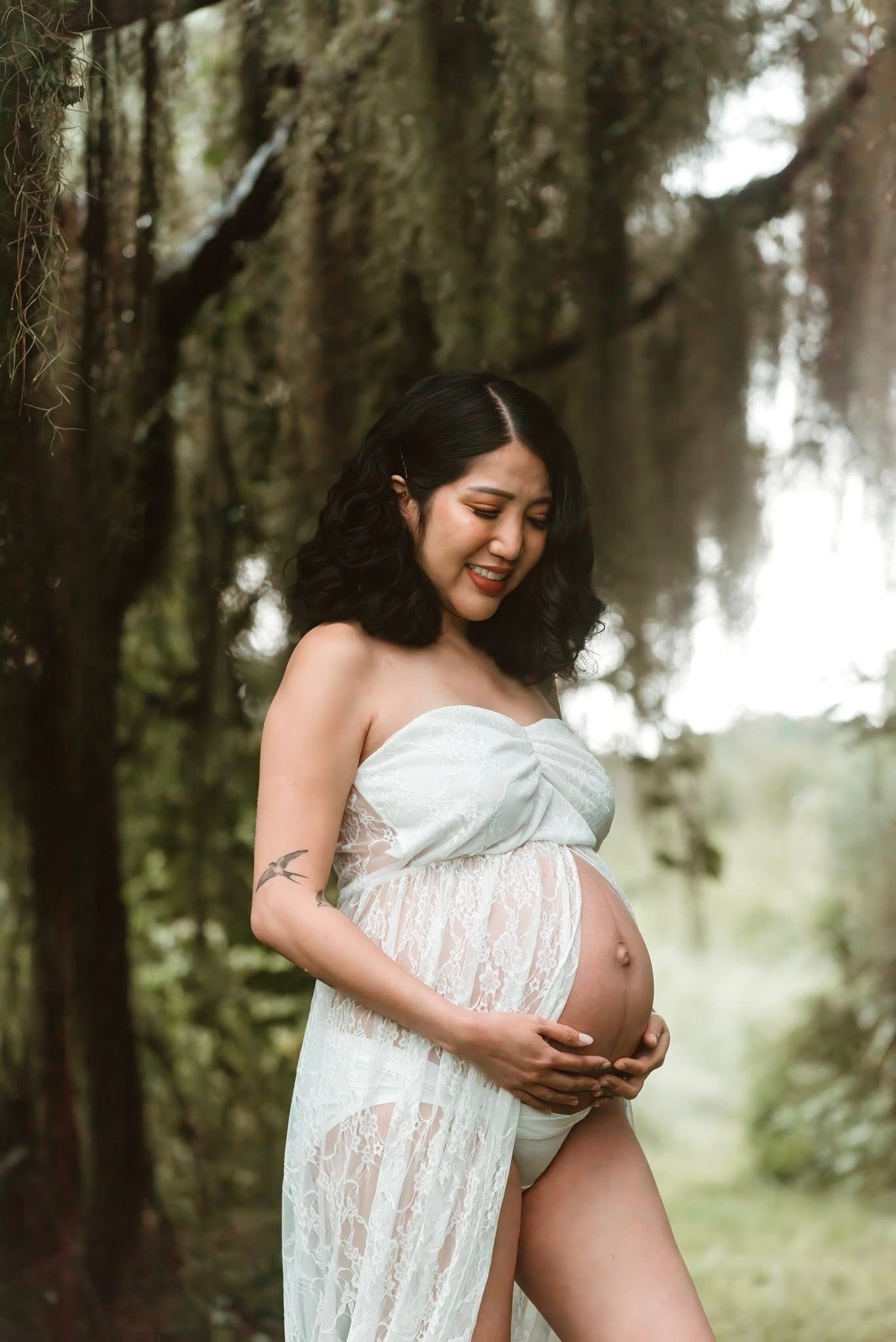 Dreamy forest maternity photoshoot with expecting mother wearing white lace fabric in a misty wooded setting.
