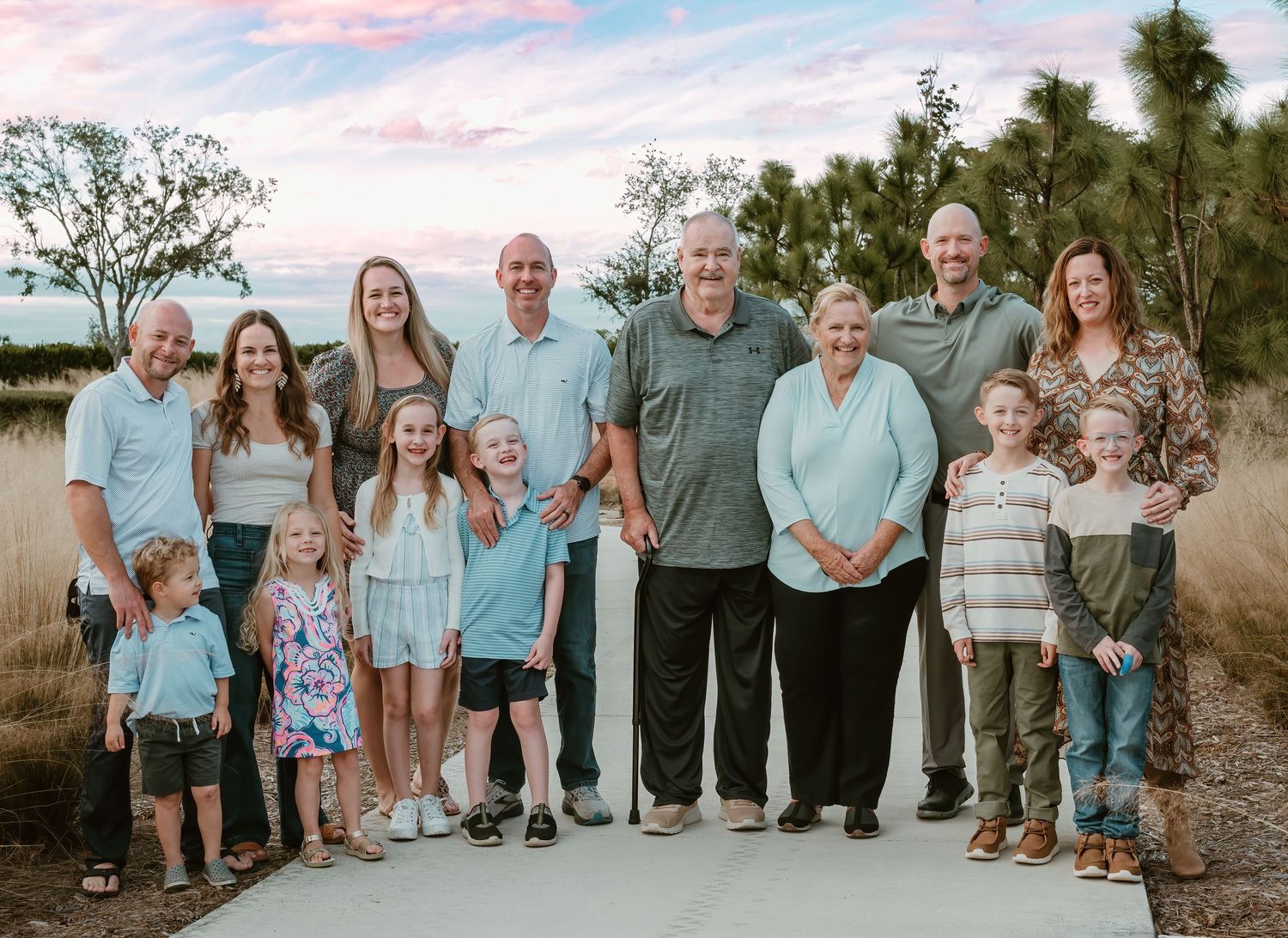 Large extended family group wearing coordinating blue and neutral outfits poses outdoors at sunset for portraits.