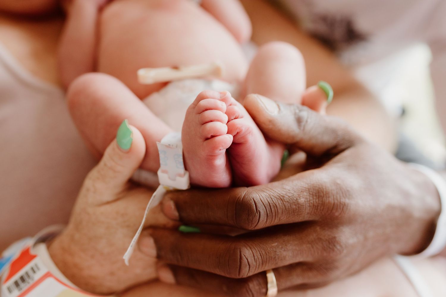 Gentle hands holding and supporting a newborn baby's tiny feet against a light background.