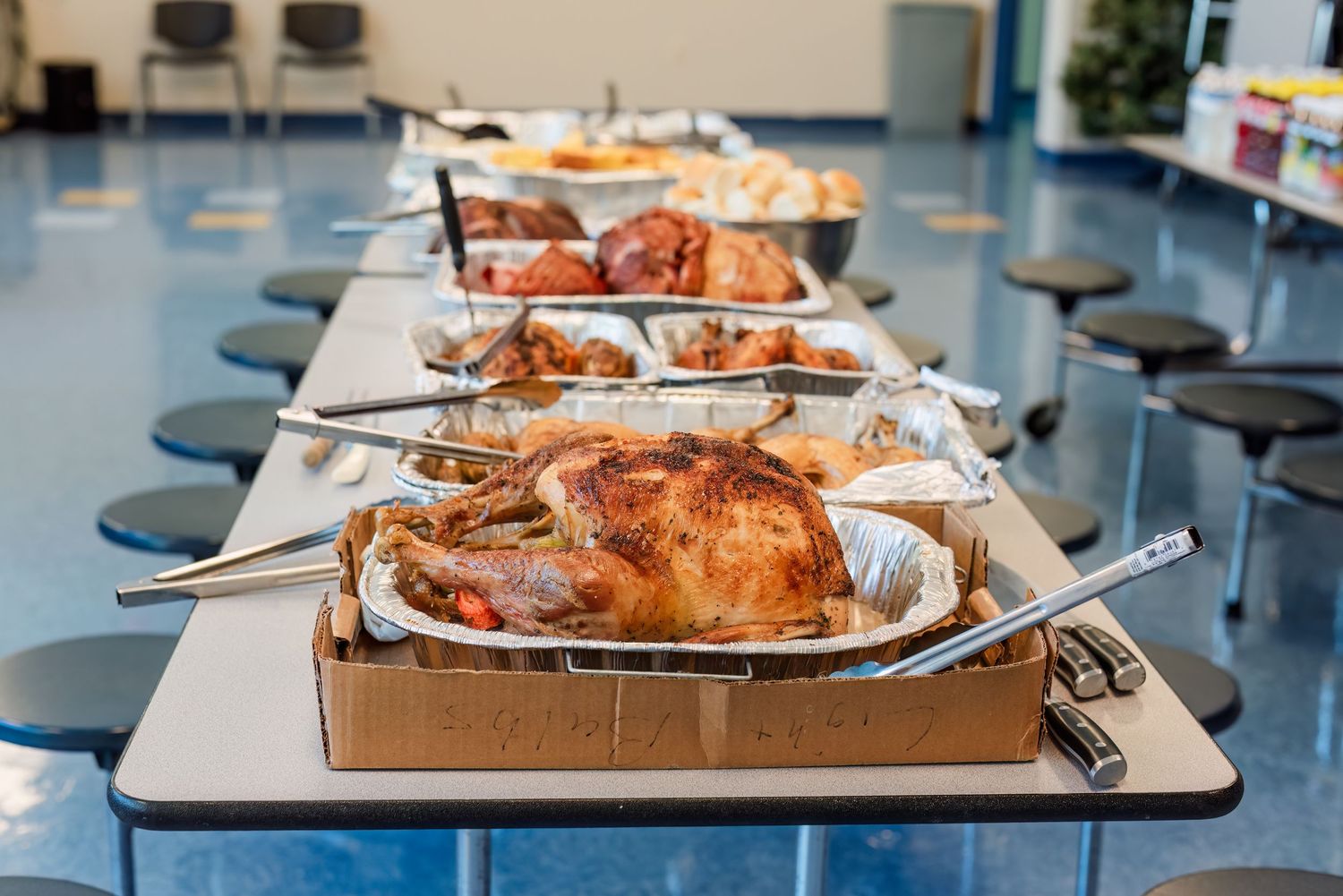 A row of golden roasted turkeys on serving platters displayed on a long table in what appears to be a dining hall.