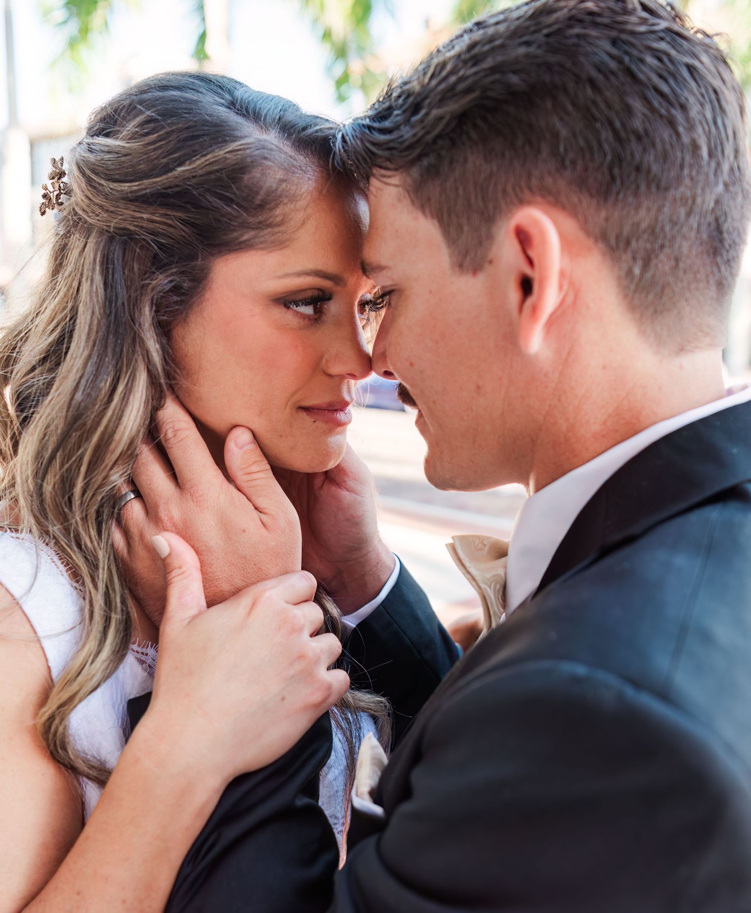 A bride and groom share an intimate moment, foreheads nearly touching, as he gently cups her face on their wedding day.
