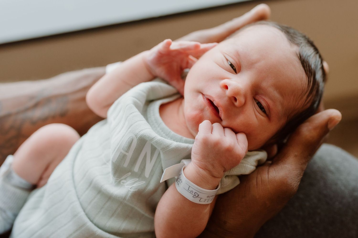 A peaceful sleeping baby wearing a light-colored onesie rests their head against a soft surface.