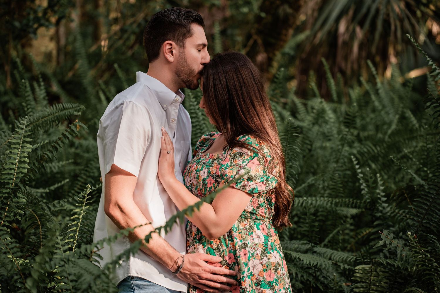 Romantic couple embraces intimately among lush green ferns in a tropical garden setting.
