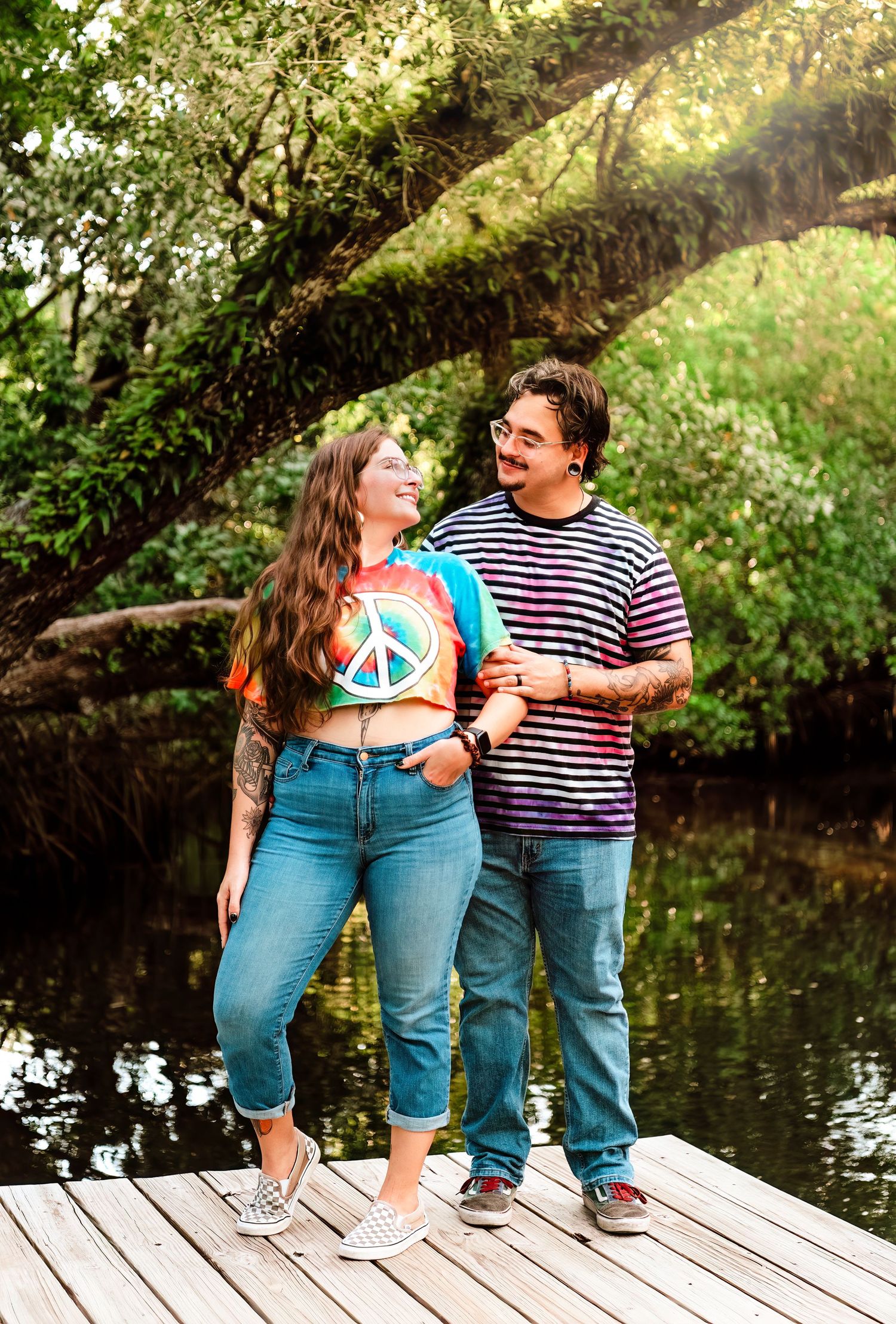A couple shares playful moments together on a wooden dock by a serene pond on a sunny afternoon.
