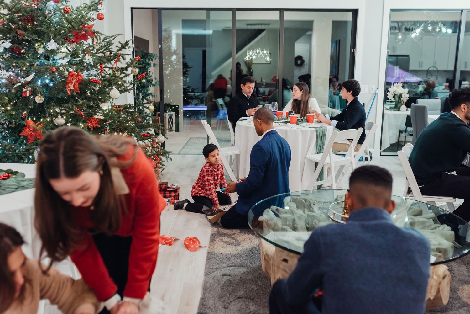 People gathered at tables for a holiday party with a decorated Christmas tree in modern office space.