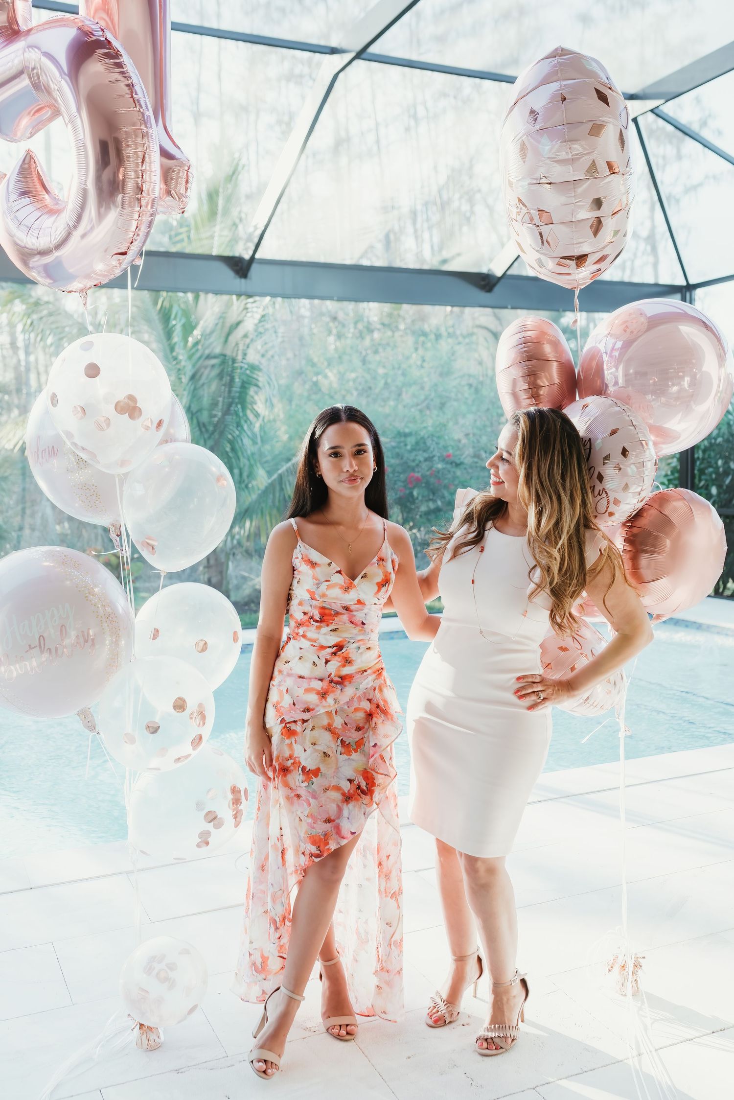 Festive celebration scene with balloons in white and coral colors featuring people in matching dresses in an airy venue.