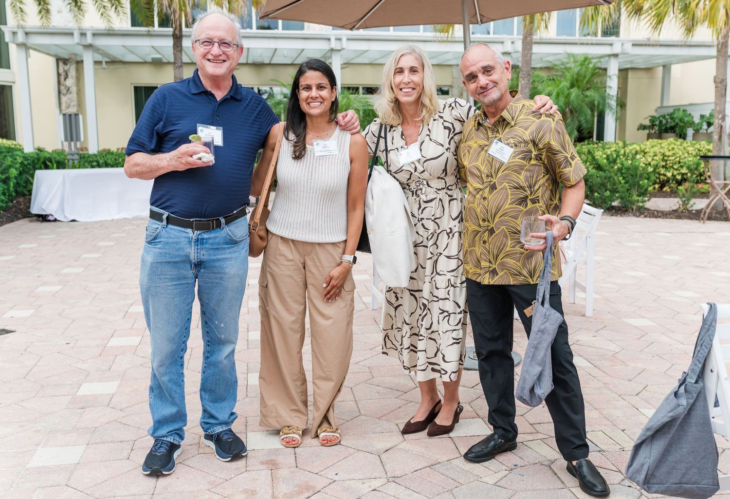 Four guests smile together at an outdoor social gathering at a tropical resort venue.