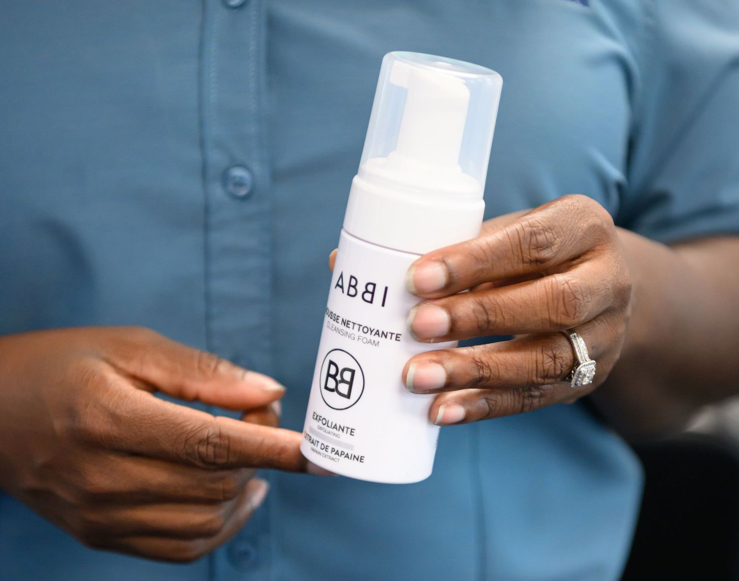 Person holding a white ABBI foaming cleanser bottle, showcasing the skincare product with elegant hands.