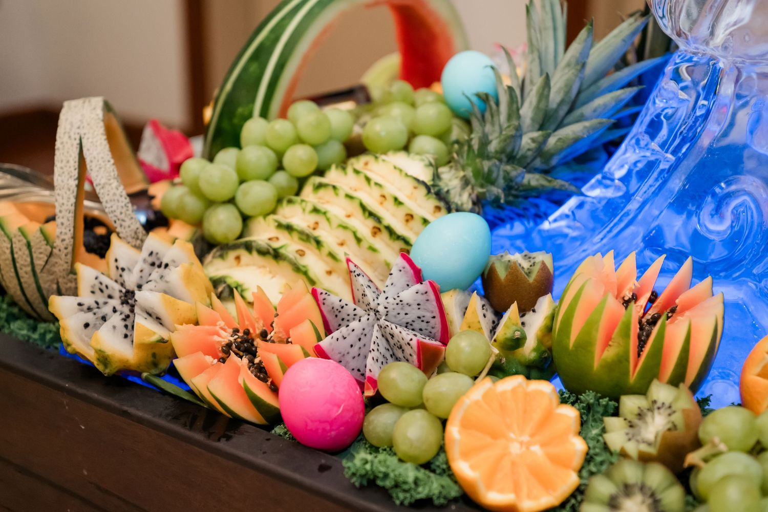 Colorful tropical fruit display with pineapple, grapes, kiwi, papaya, and dragon fruit arranged on a decorative platter.