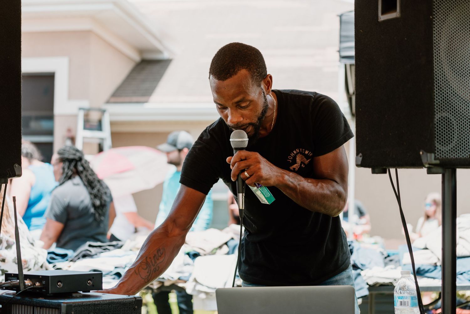 A person in a black t-shirt performs as a DJ at an outdoor event with speakers and equipment set up.