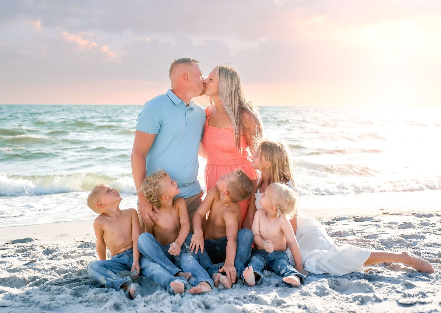 A group enjoys a sunset photoshoot together on a white sandy beach with waves crashing behind them.