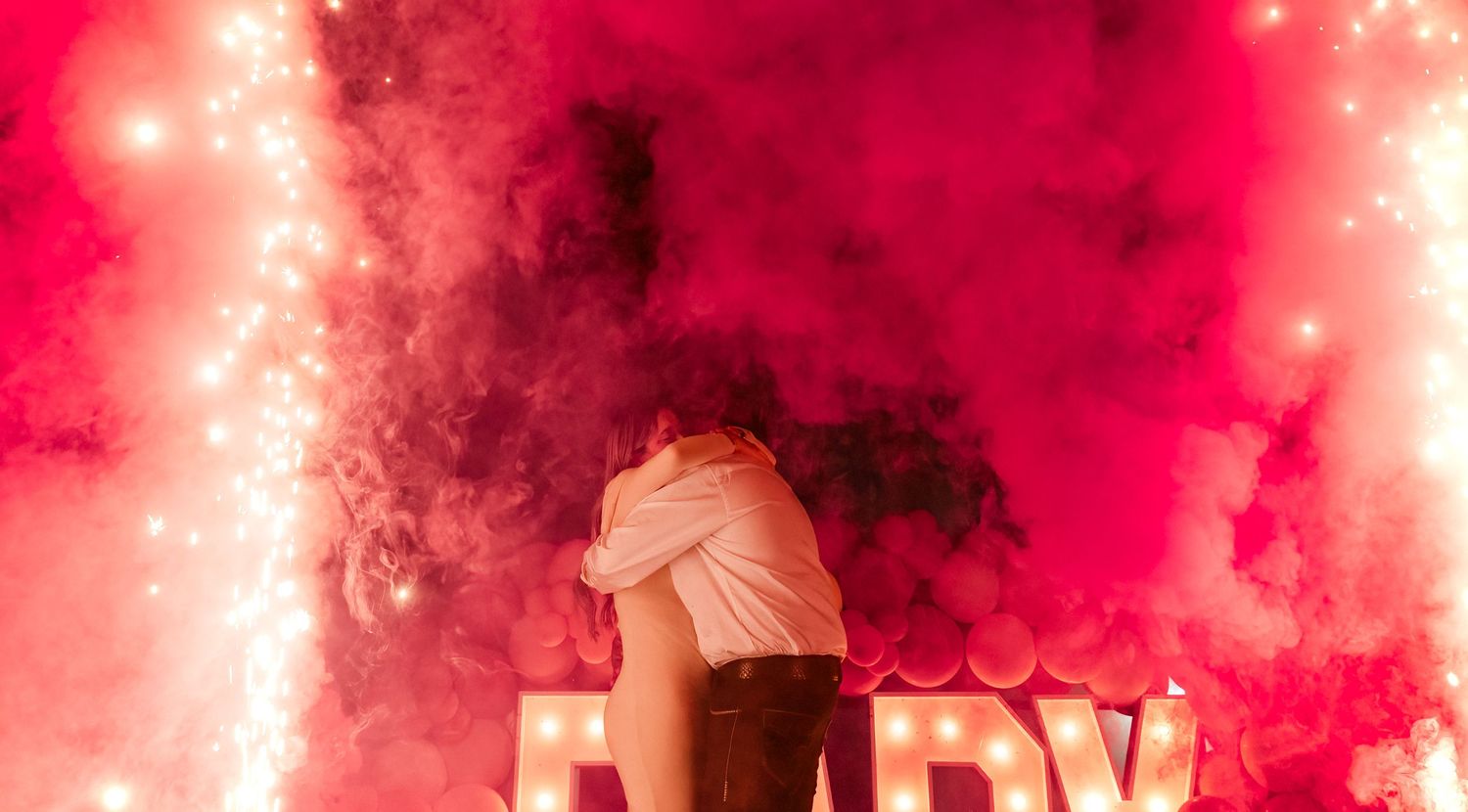 Red smoke fills the air during a dramatic outdoor performance with silhouetted figures visible through the haze.