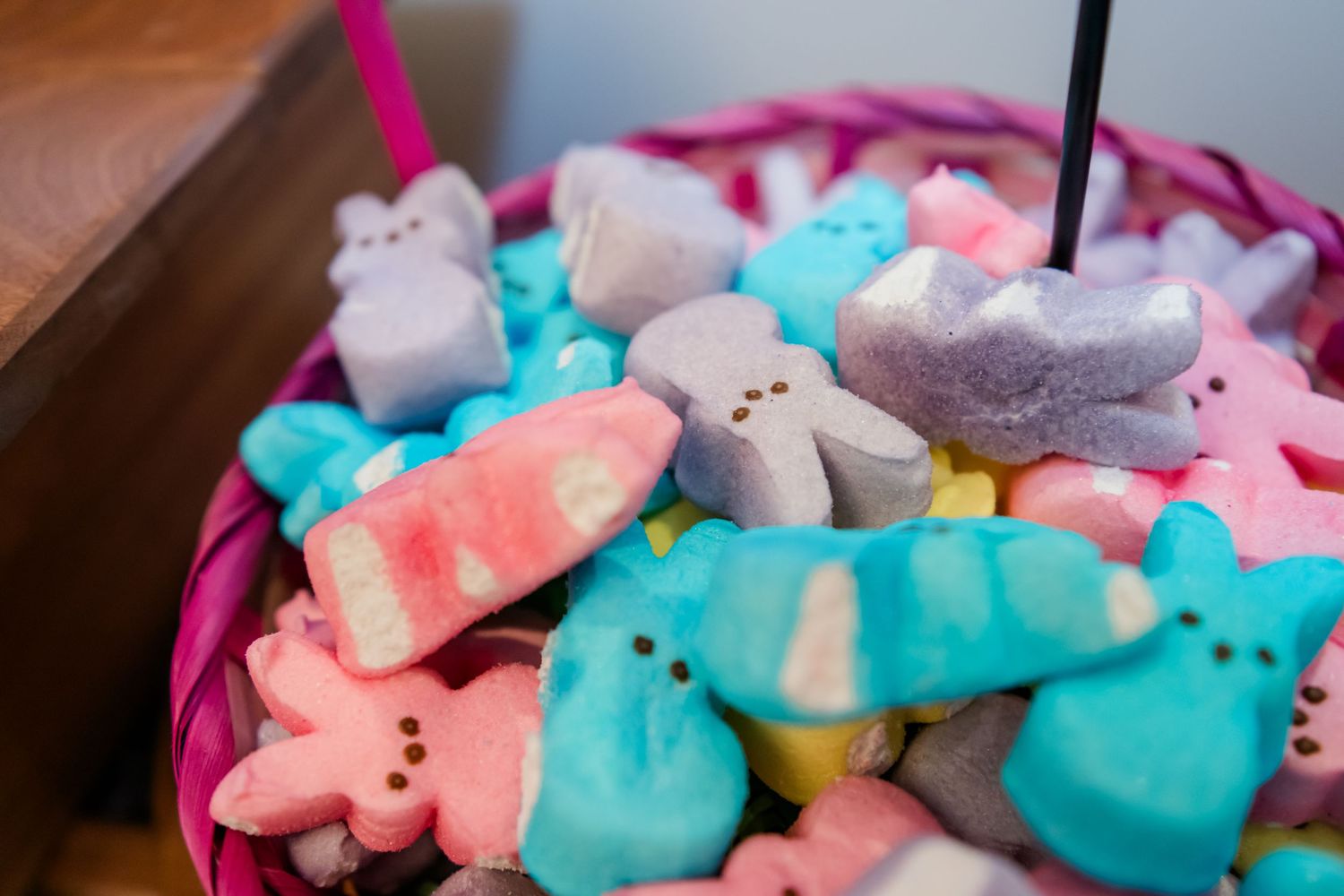 Colorful Easter Peeps marshmallow candies in pink, blue, and gray shapes piled in a pink wicker basket.
