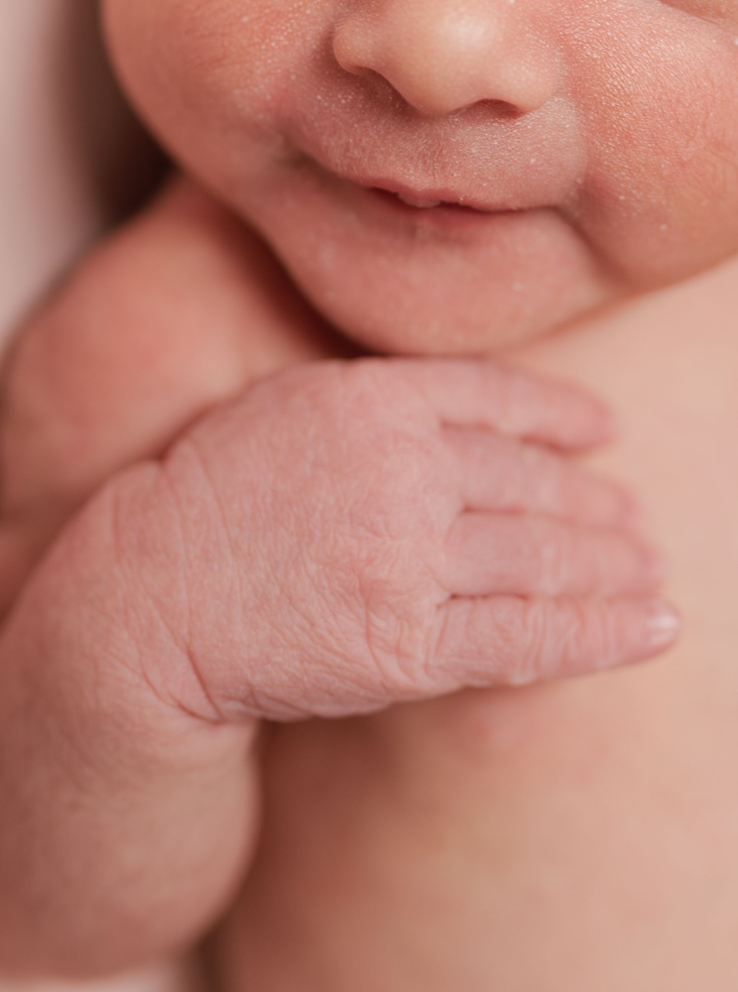 Close-up of a newborn baby's tiny wrinkled hand resting against their chin and chest.
