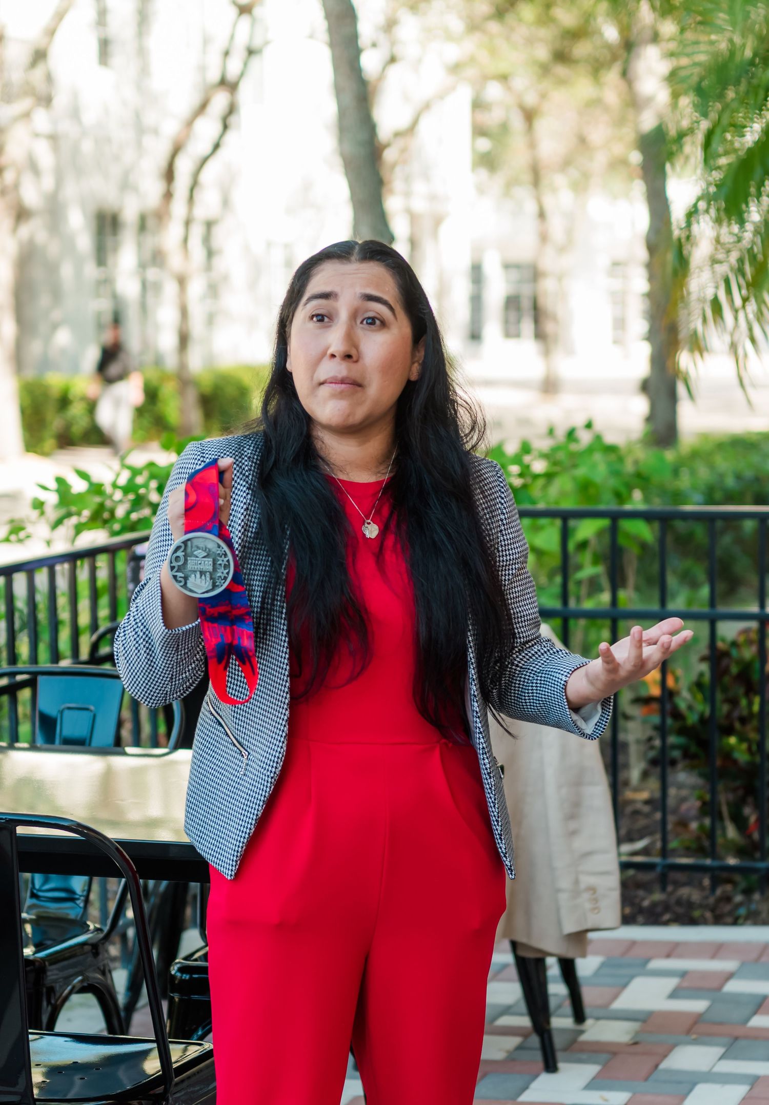 Person in a bright red outfit and gray cardigan poses outdoors on a patio with greenery in the background.