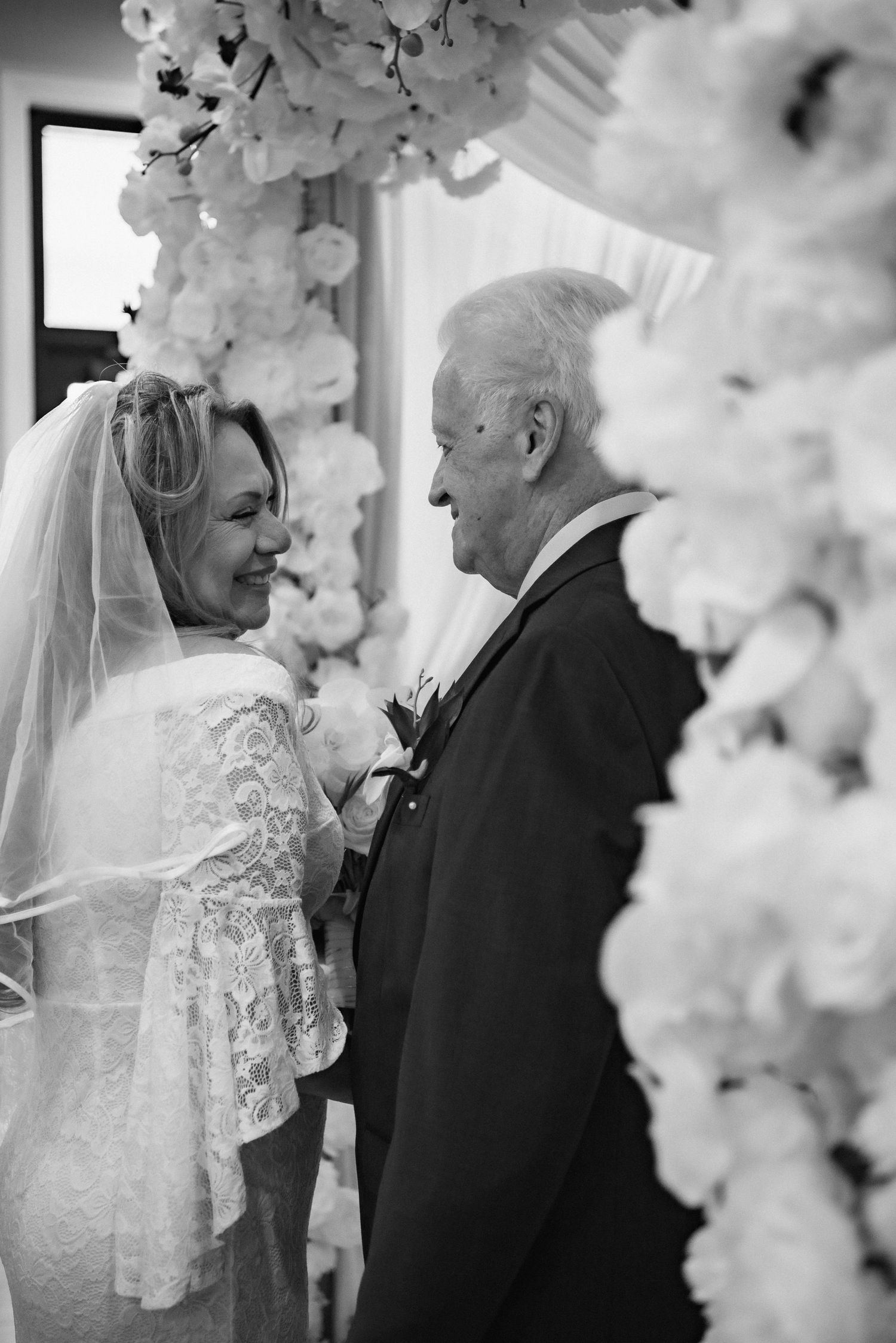 Tender black and white wedding moment framed by delicate white floral arch decorations.