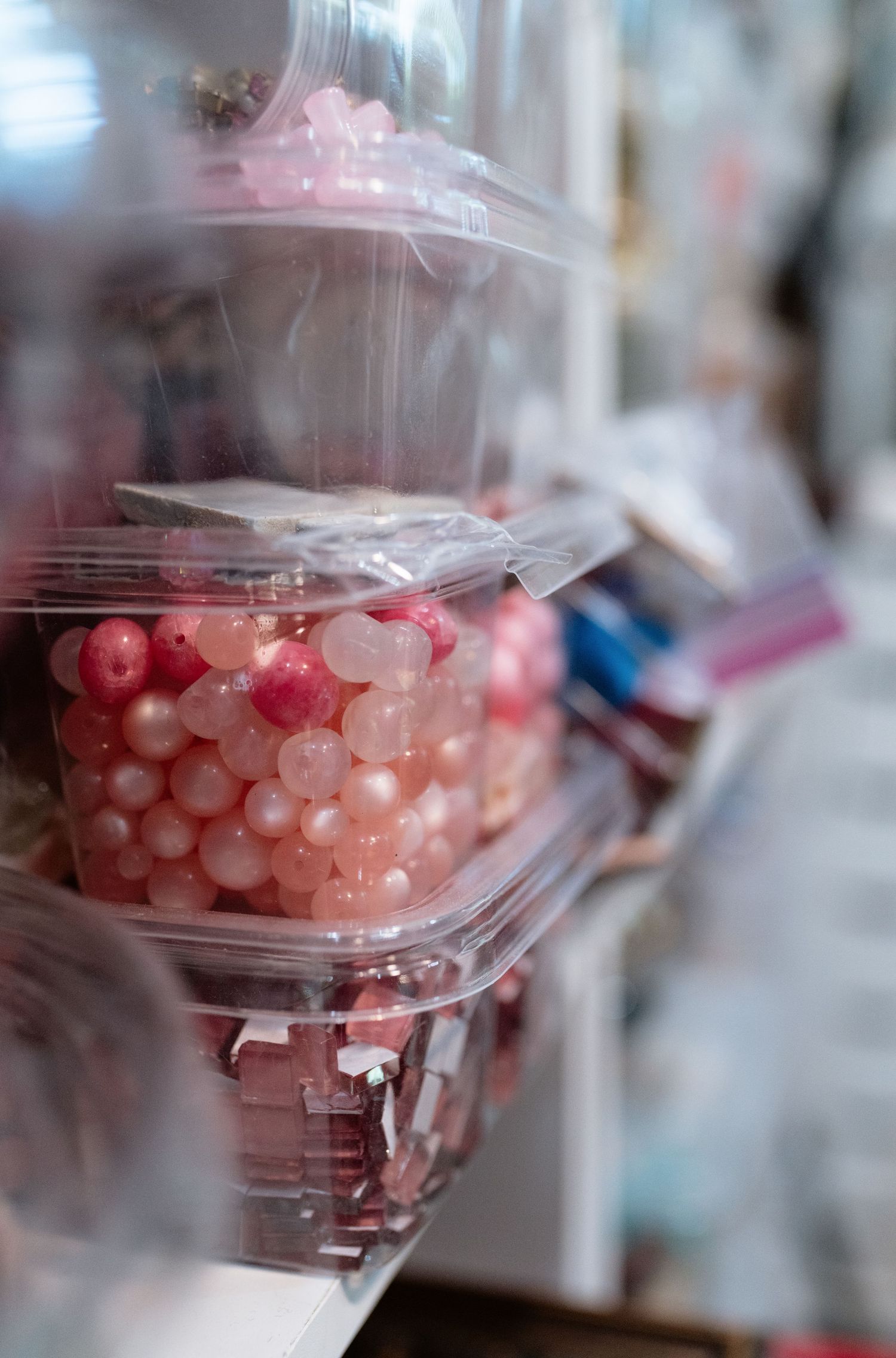 Pink and rose-colored round beads in clear plastic containers stacked on a craft supply store shelf.