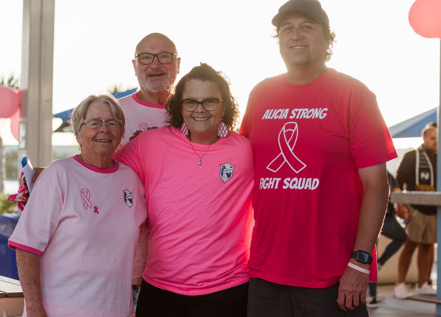 A group wearing pink shirts poses together at a breast cancer awareness event.