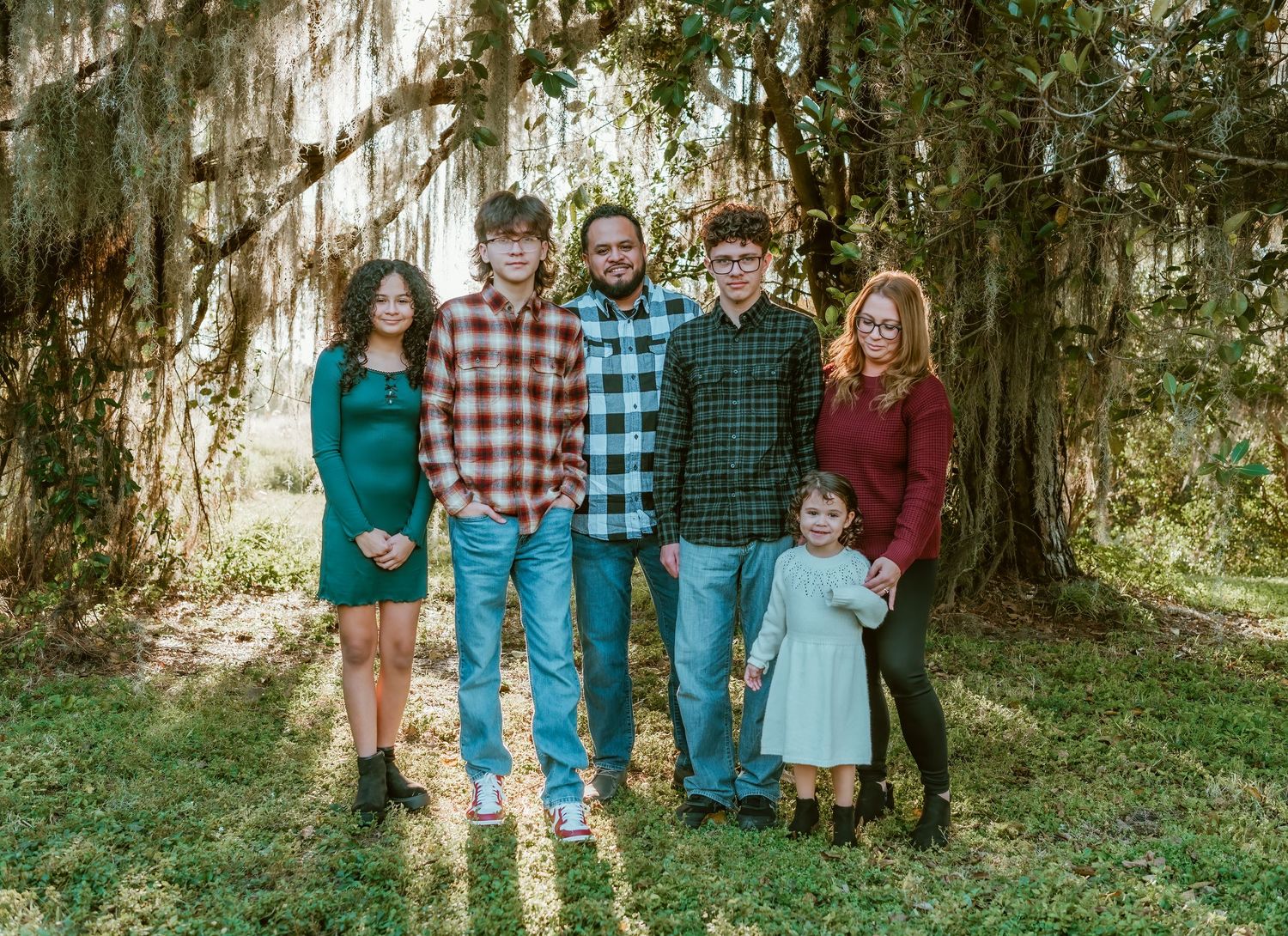 A group stands together in front of hanging tree branches in a natural outdoor setting.