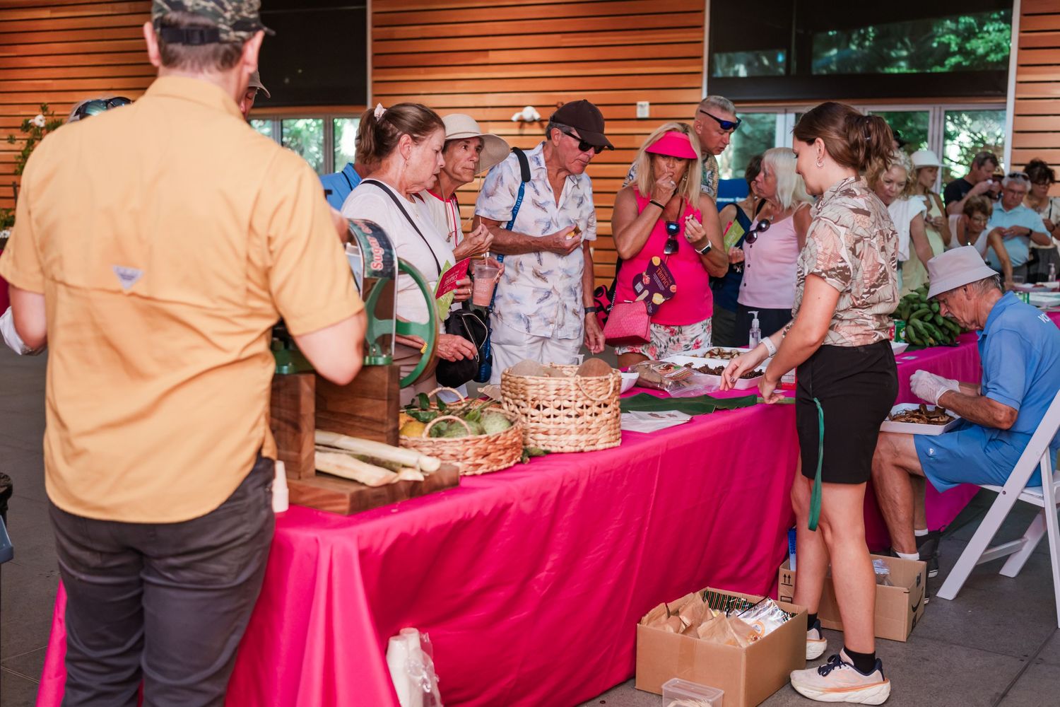 People browsing a buffet table with pink tablecloth at an outdoor community food event.