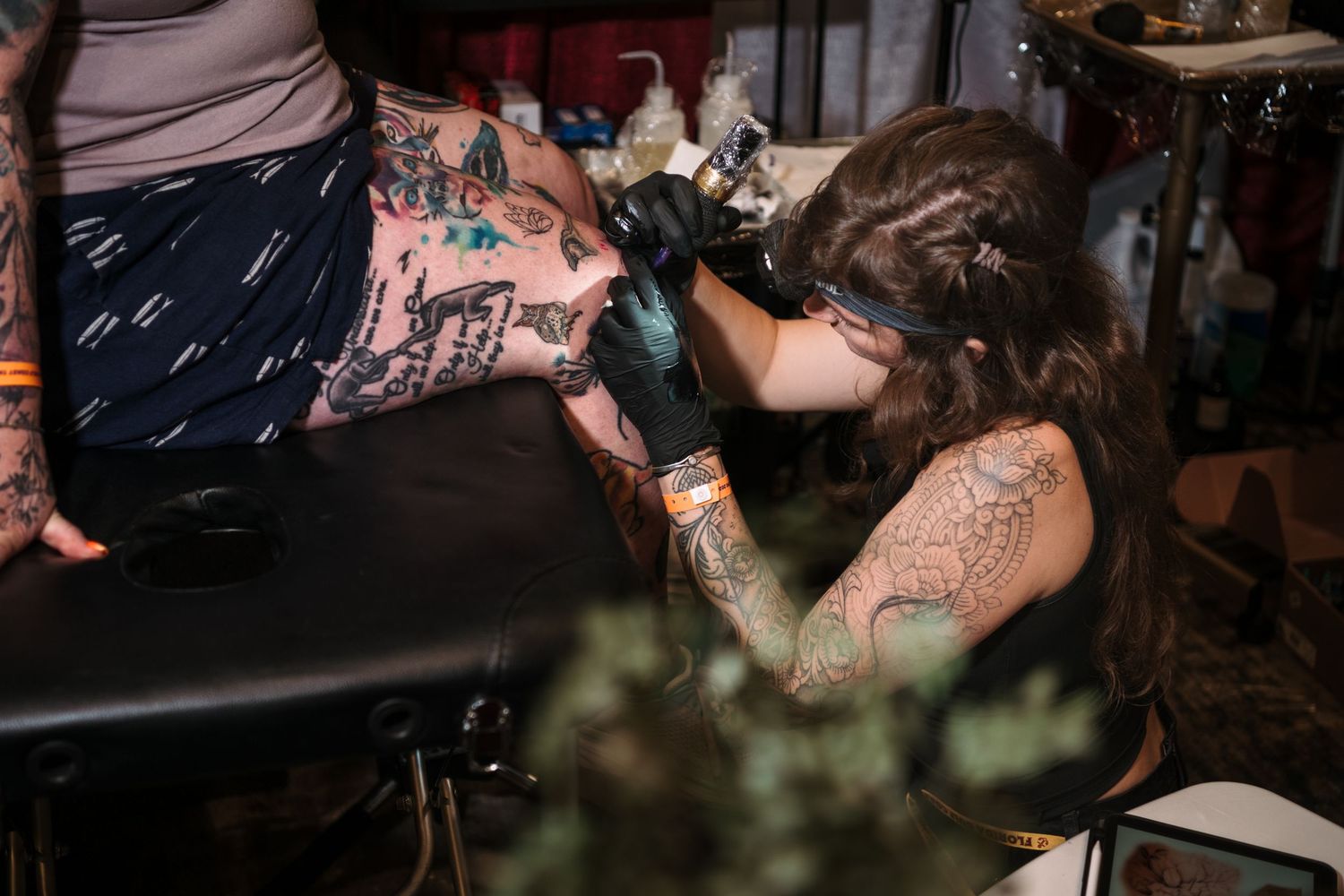 Tattoo artist with dreadlocks and tattoos carefully inking a client's arm at a tattoo convention.