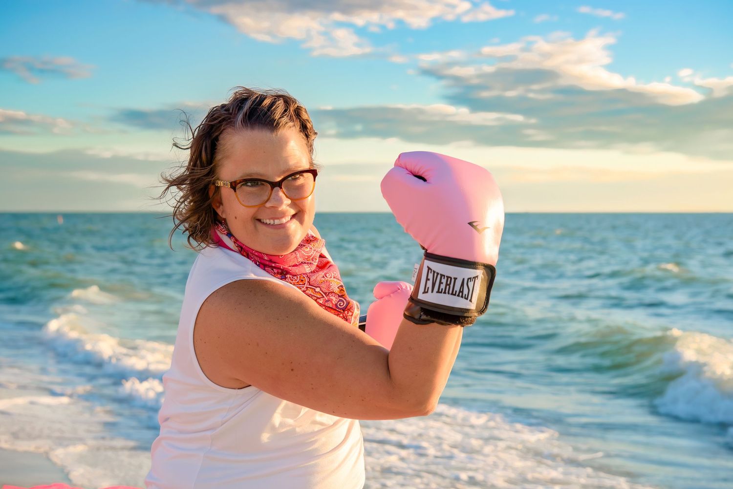 A boxer trains with pink gloves on a scenic beach at sunset with waves crashing in the background.