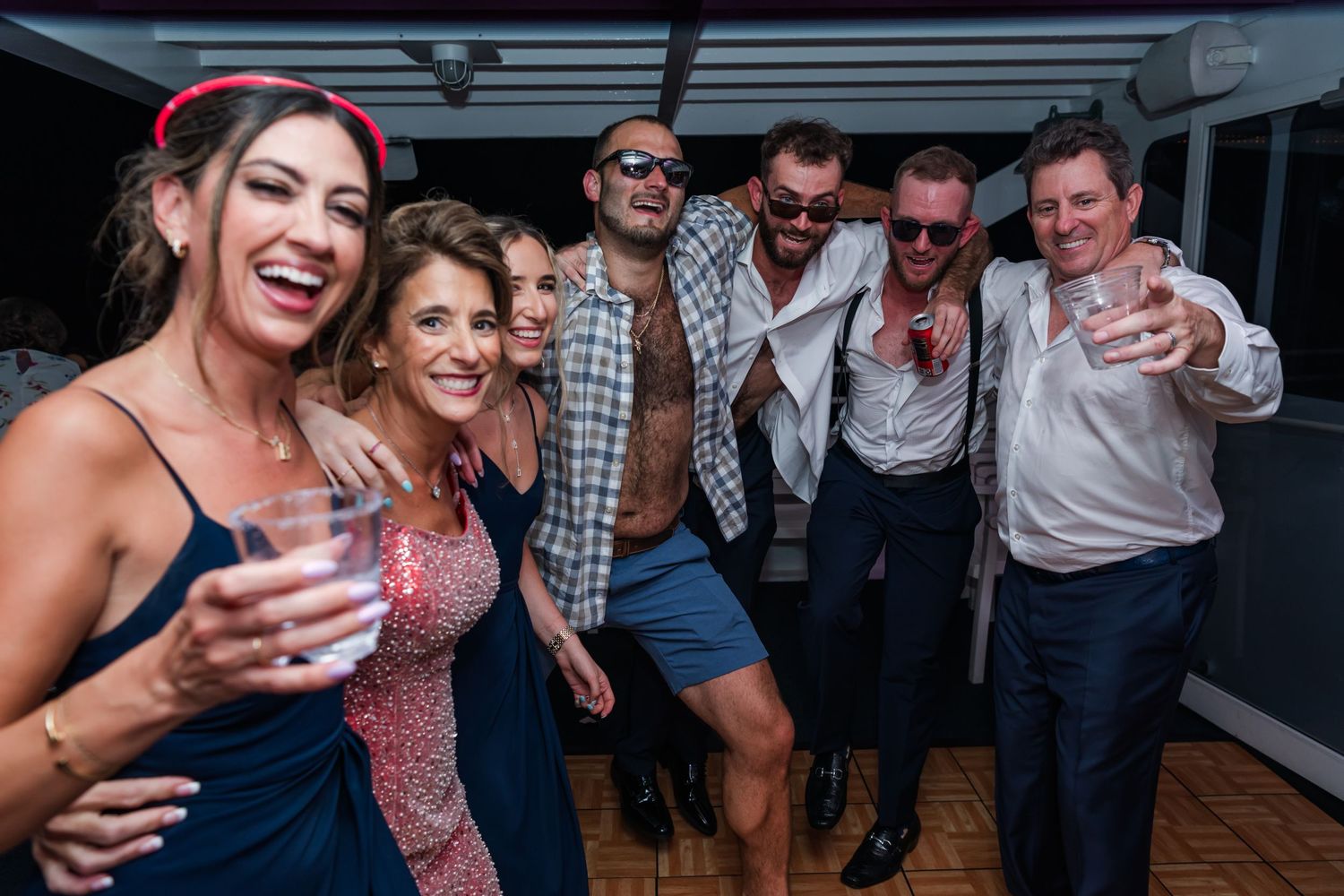 Group of friends laughing and posing with drinks at a lively party event on a boat deck.