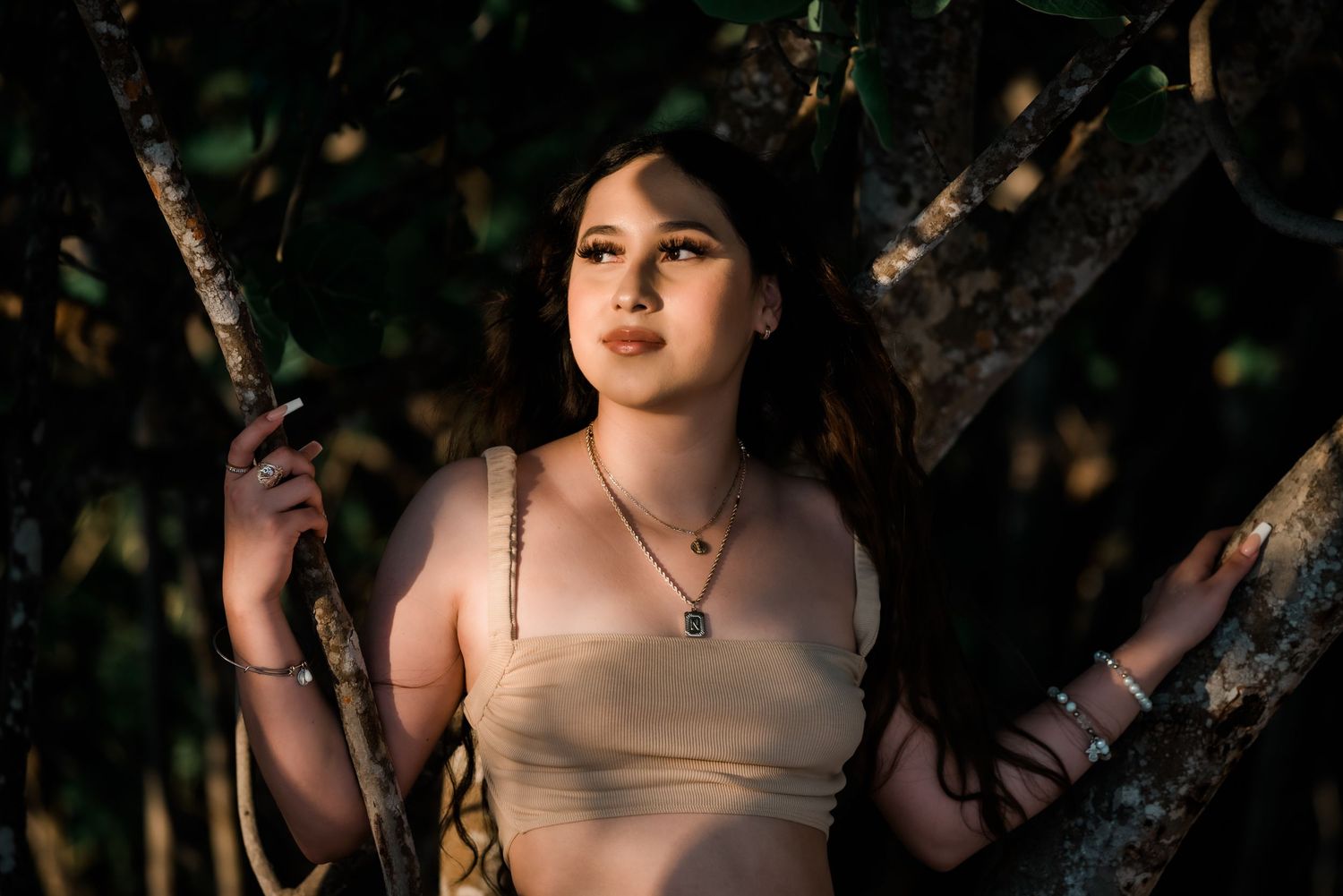 Dark romantic portrait of a person against trees with sunlight filtering through the branches creating a moody atmosphere.