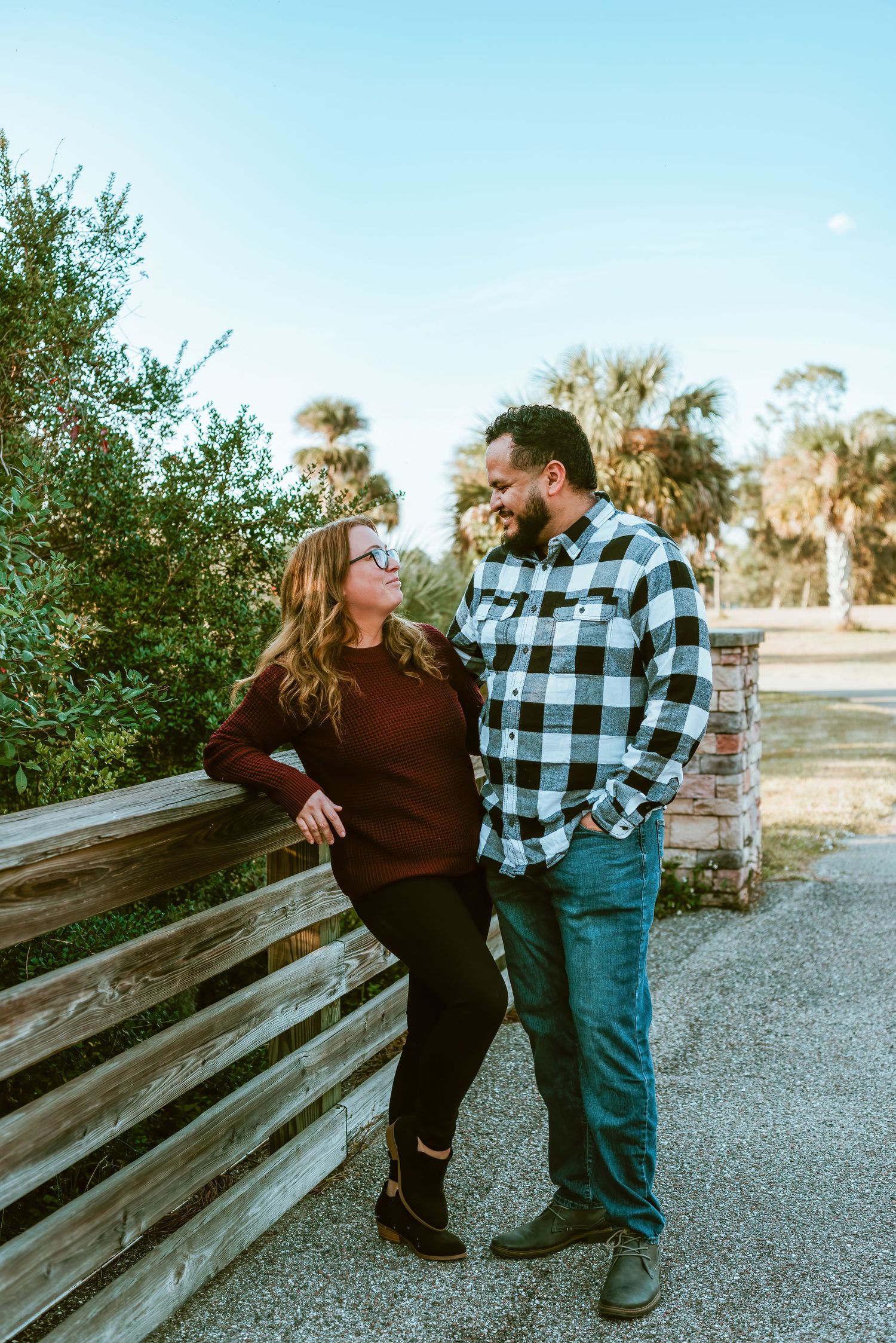 Two people share an intimate moment while leaning against a wooden fence in a park setting during golden hour.