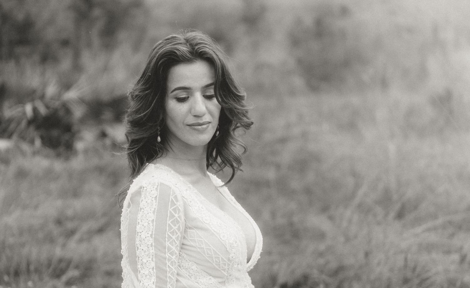 Black and white portrait of someone wearing a white knit sweater while standing in a dreamy outdoor setting.