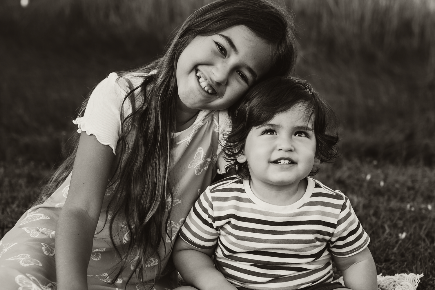 Candid black and white photo of two people sitting together on grass, one wearing a striped shirt, sharing a joyful moment.