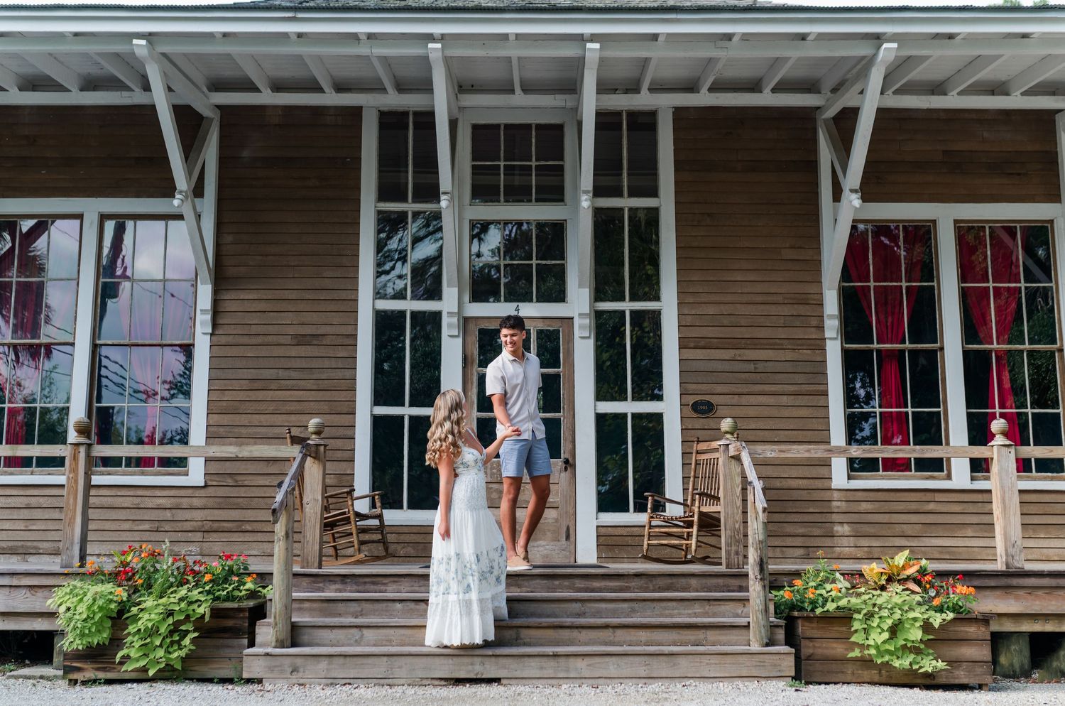 Couple standing on wooden porch steps of a rustic venue, bride in white lace gown, groom in casual attire.