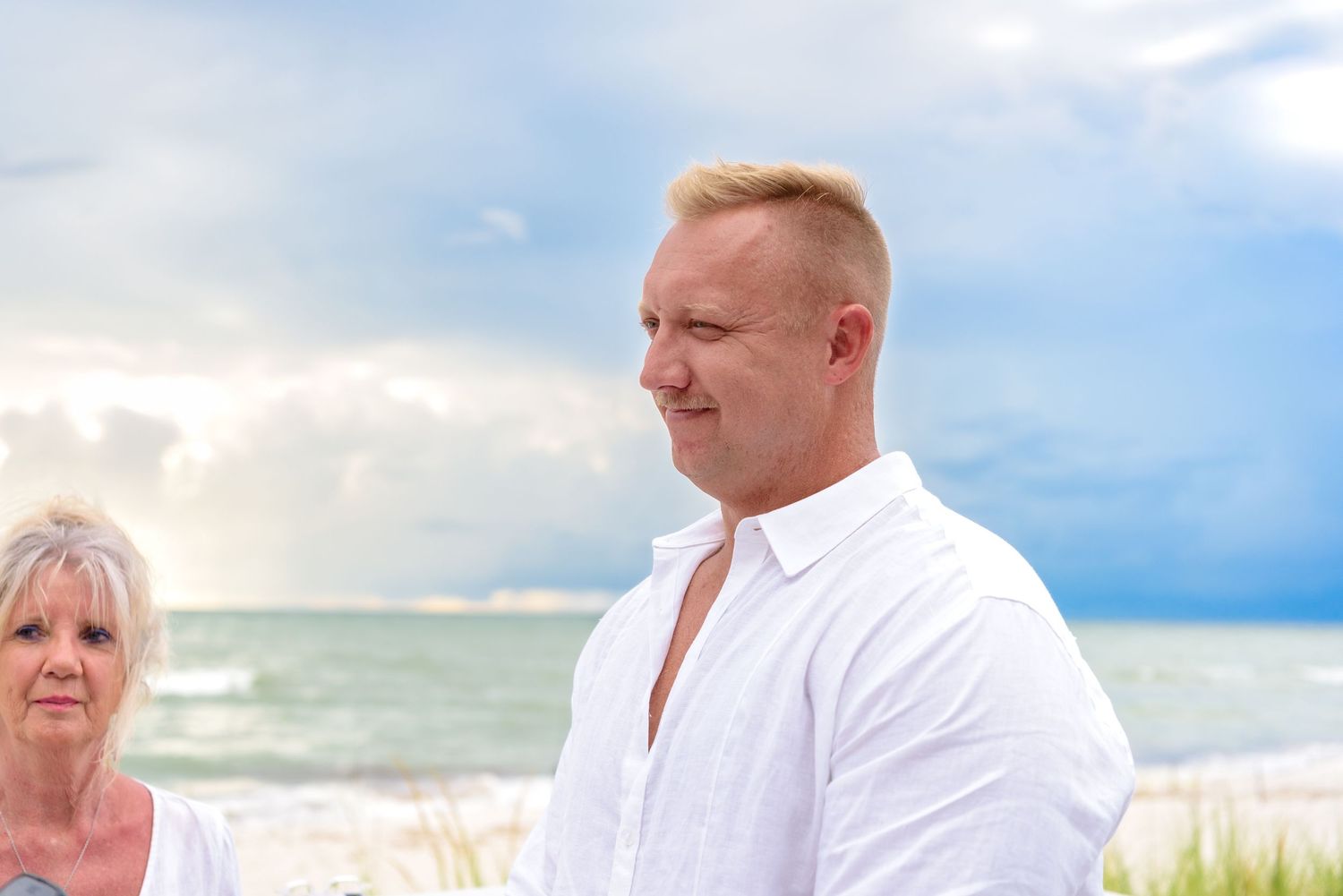 A couple in white attire walks along a tropical beach during a photo session at sunset.