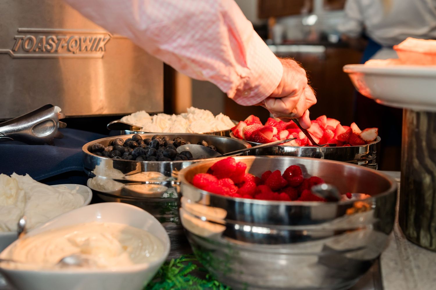 Chef arranging fresh strawberries and blueberries in metal bowls at a buffet food station.