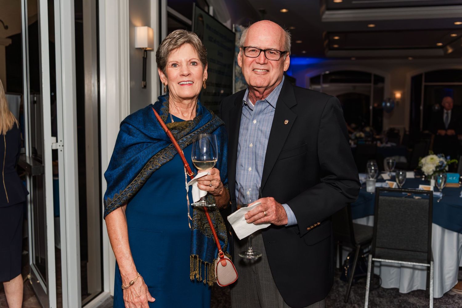 A couple in formal attire at an evening event, with the woman in a blue dress and man wearing a dark blazer.
