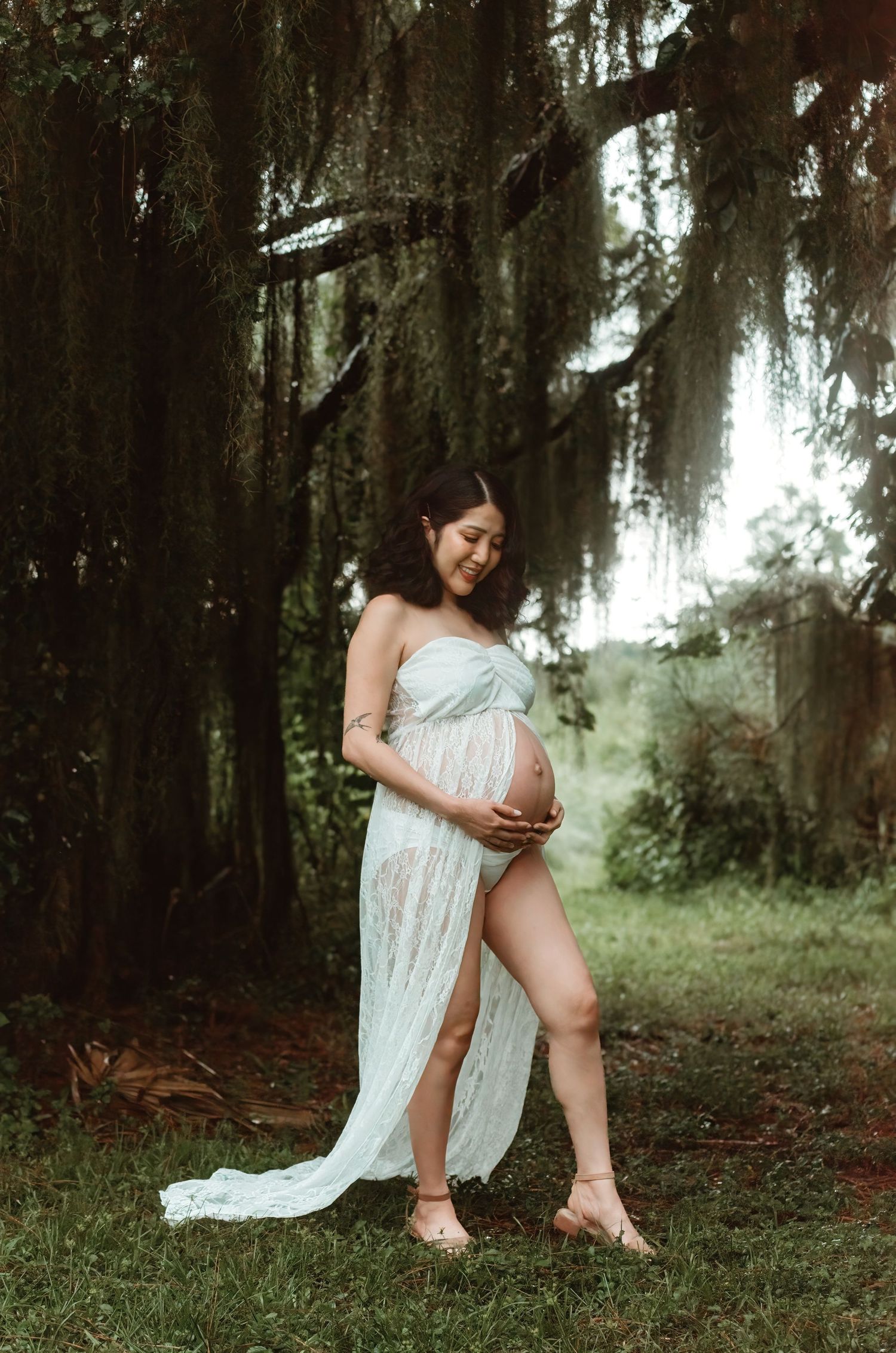 A dreamy maternity photoshoot in a mossy forest setting with Spanish moss hanging from trees in soft natural lighting.