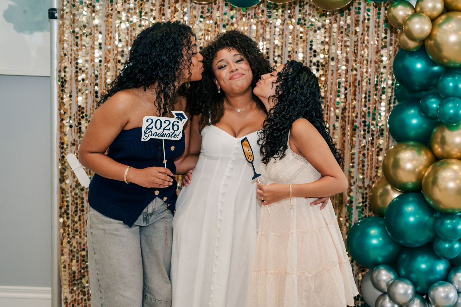 Three women pose together at a New Year 2026 party with gold and teal balloon decorations.
