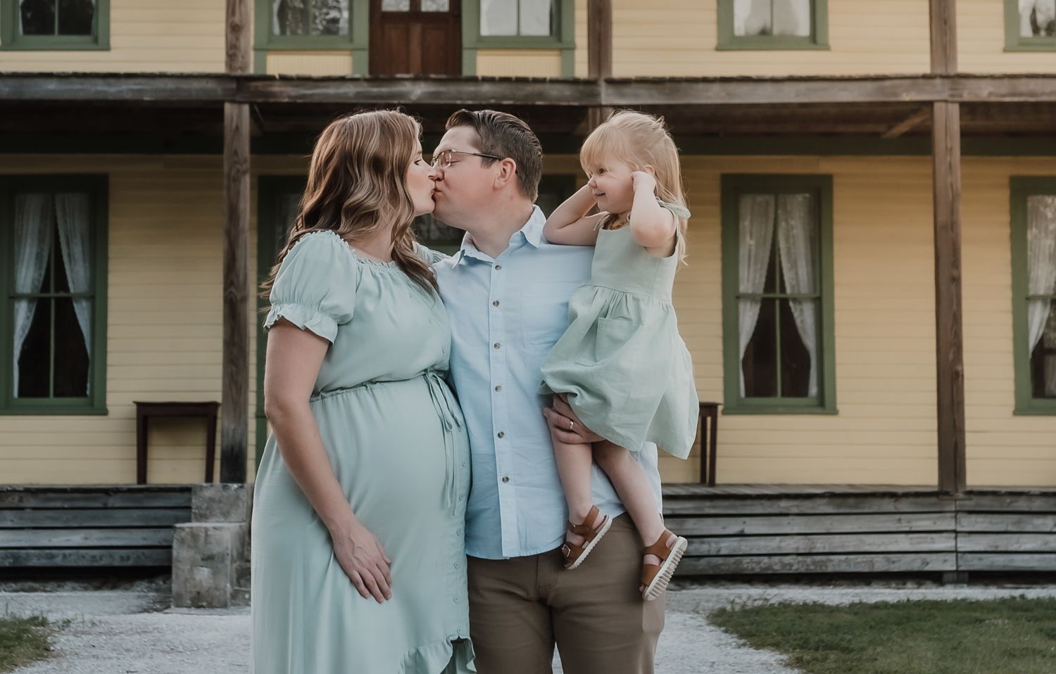 Couple in coordinated blue and mint outfits embrace lovingly on the porch of a historic building.