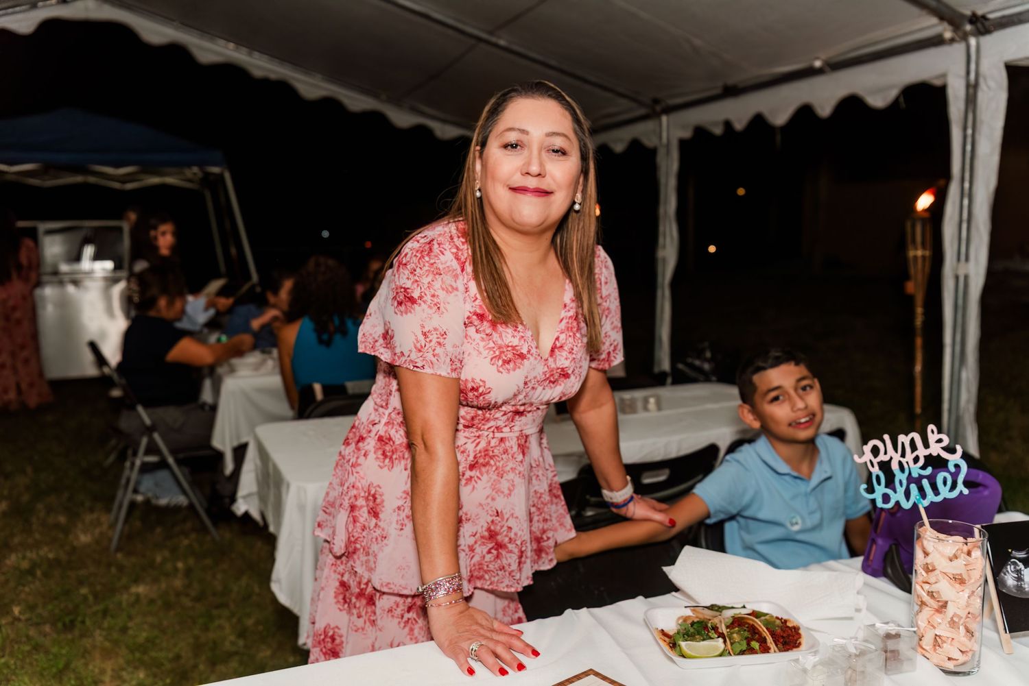 A group of people gathered at an outdoor event under a white tent enjoying a meal together.