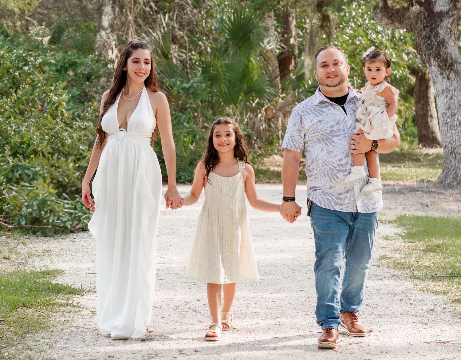 A family walks together on a dirt path through nature wearing coordinated white and beige outfits.
