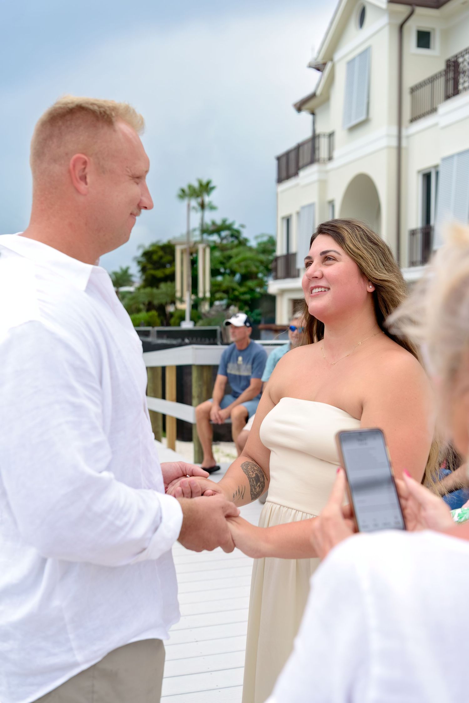 A couple in white attire dances together on a beachfront balcony during a romantic celebration.