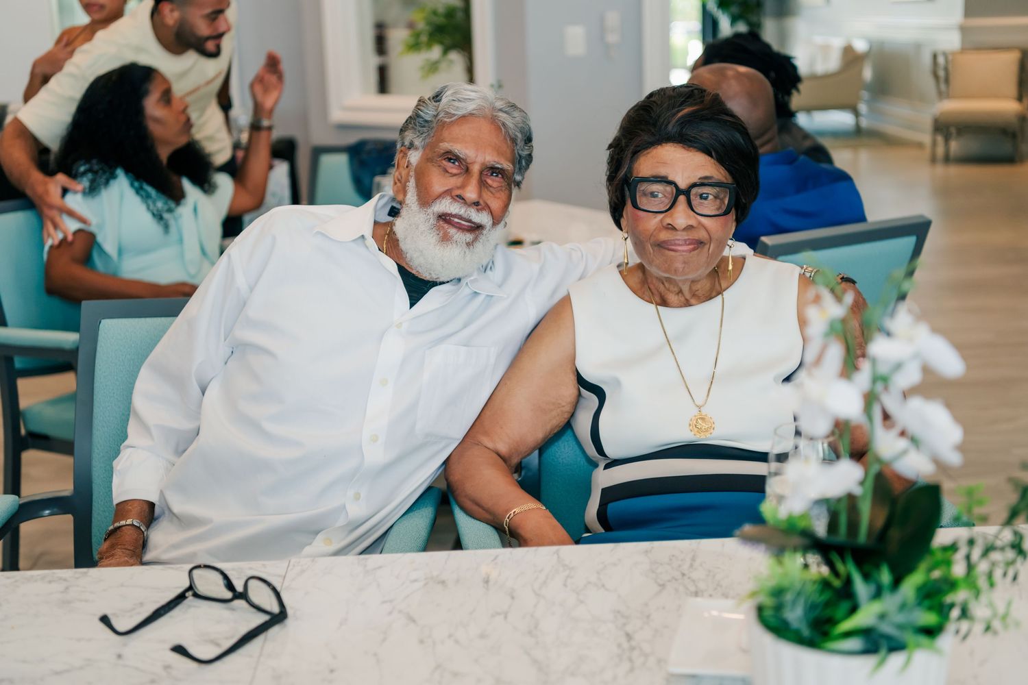 Elderly couple smiling together at a table during a celebration event in a bright, modern venue.
