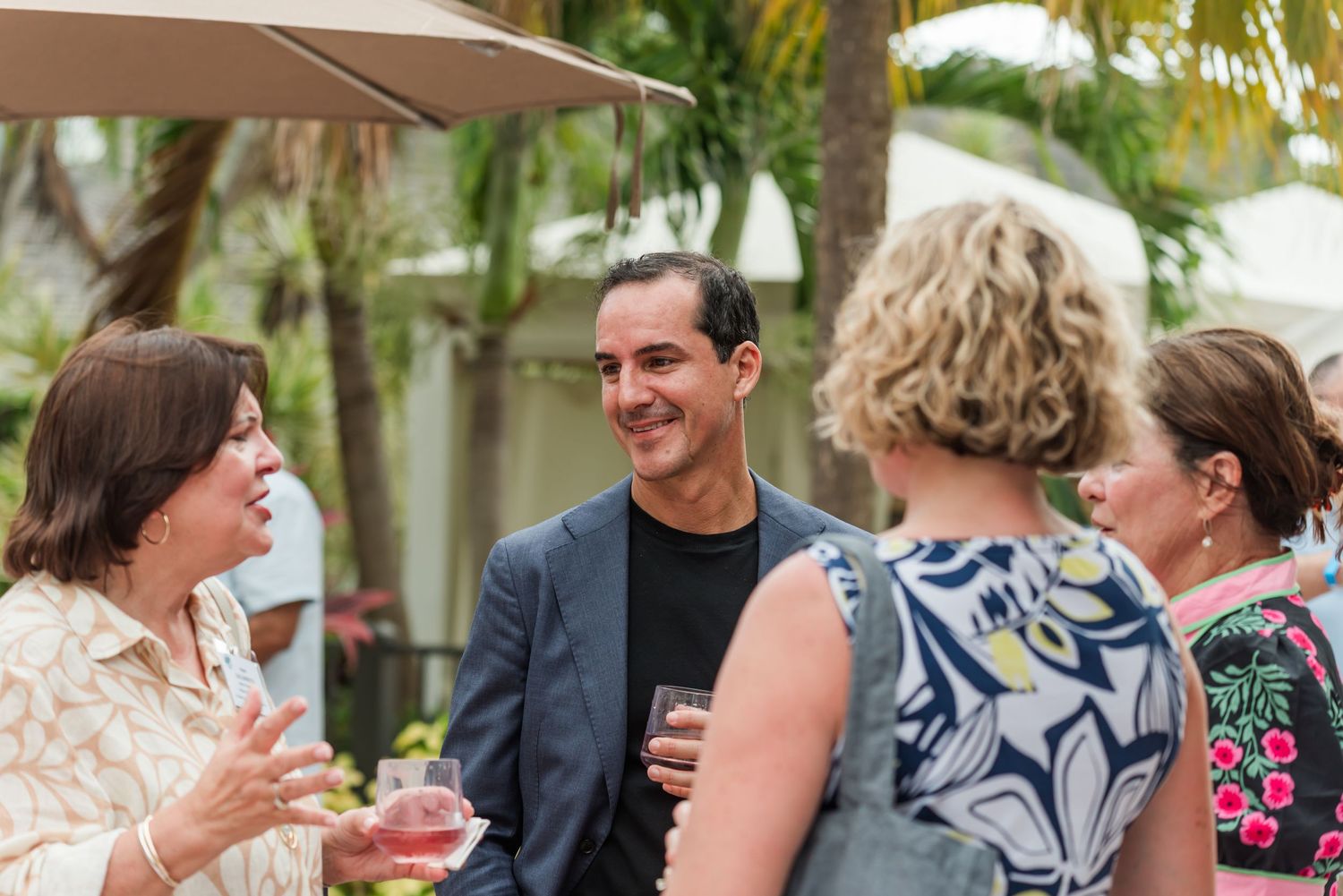 Group of adults socializing outdoors at a tropical garden party, smiling and holding drinks.