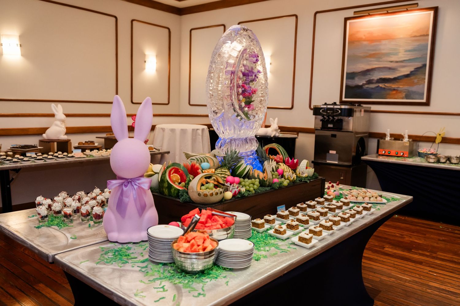 Easter-themed buffet table with a decorative ice sculpture, bunny figurines, fresh fruit, and assorted desserts.