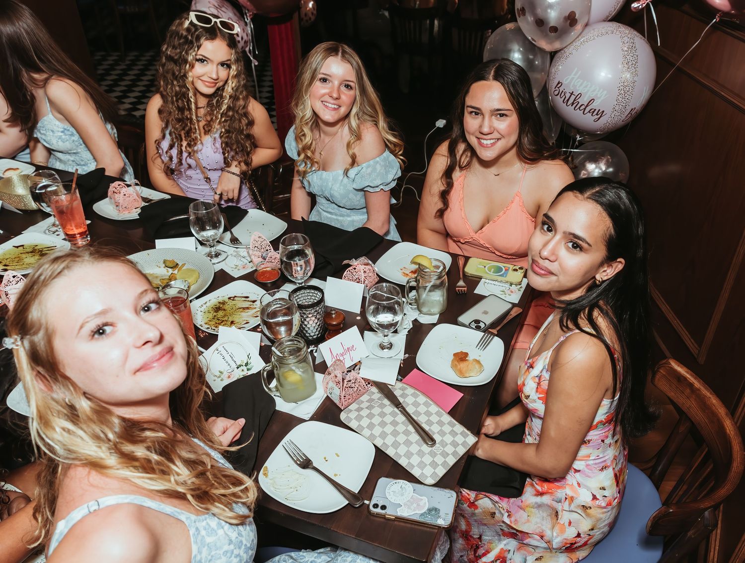 A group of friends enjoying dinner at a restaurant table with balloons and place settings for a celebratory gathering.