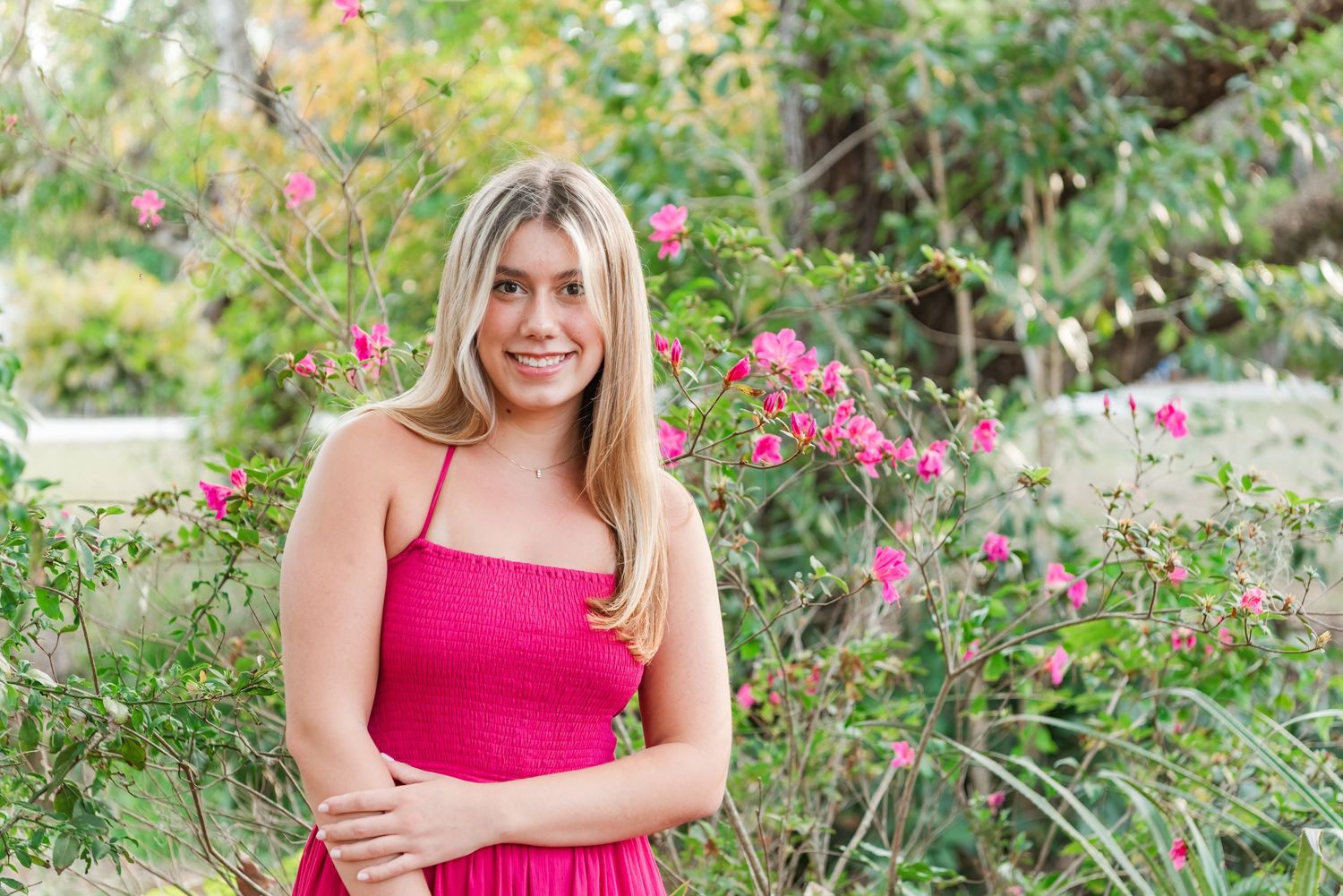 Person in a bright red dress poses among vibrant flowers and greenery in an outdoor garden setting.