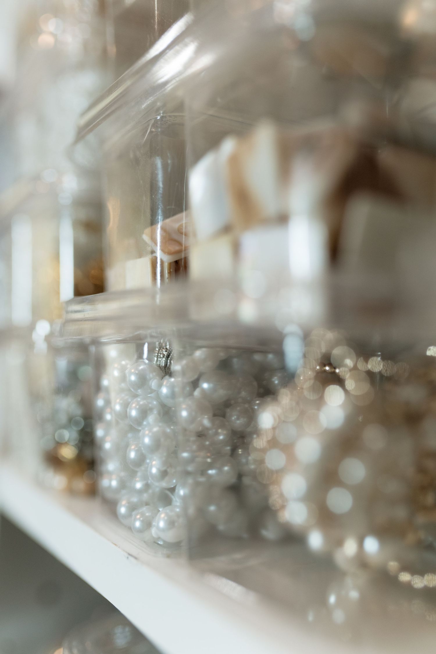 White shelves display glass jars filled with pearl beads and decorative items in soft bokeh lighting.
