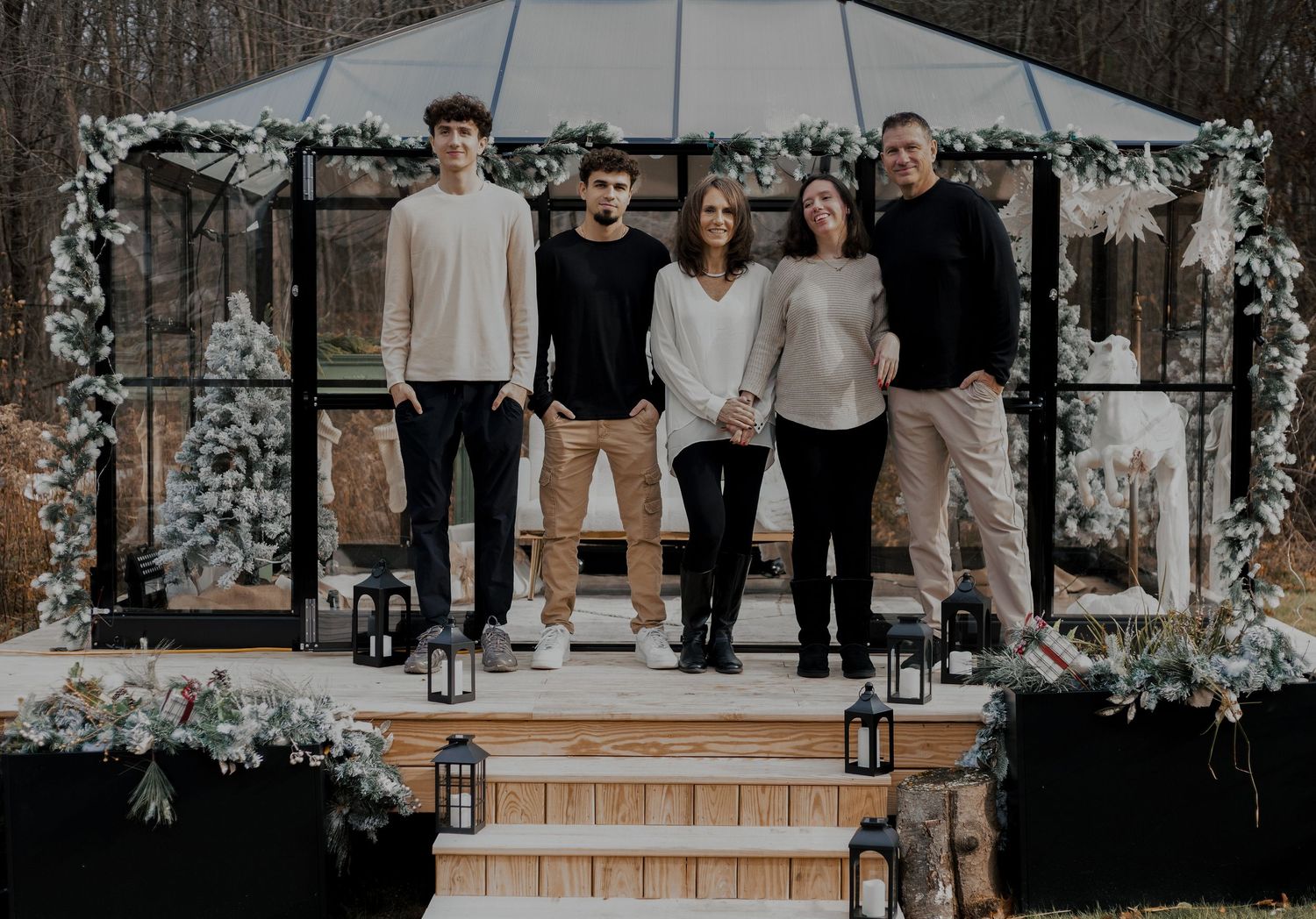 A group poses together on wooden steps decorated with lanterns and winter greenery.