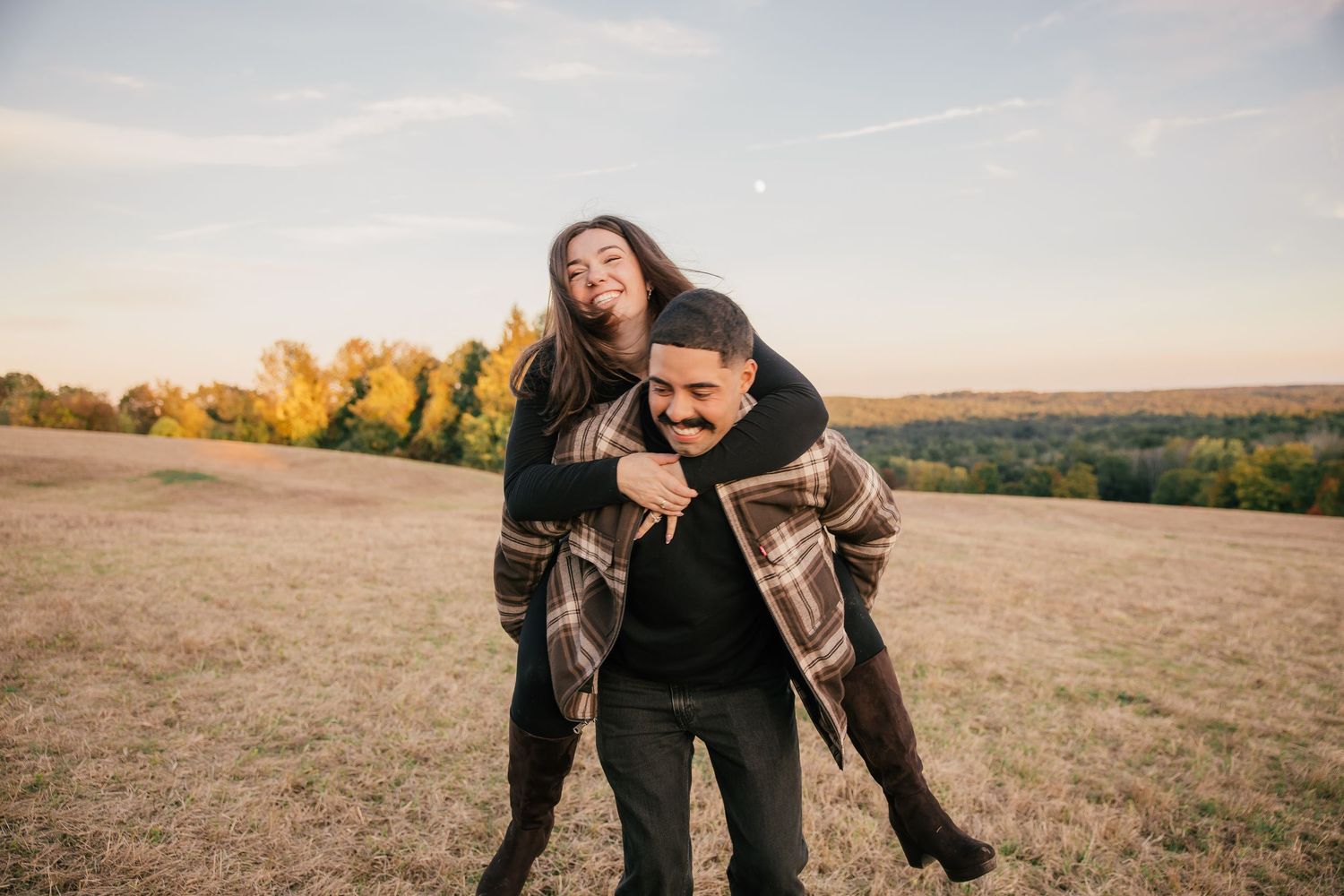 A joyful couple sharing a piggyback ride in an open field during golden hour in autumn.
